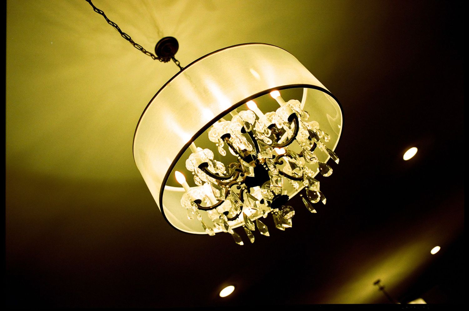 Elegant drum shade chandelier with crystal accents hanging from ceiling in warm golden light.