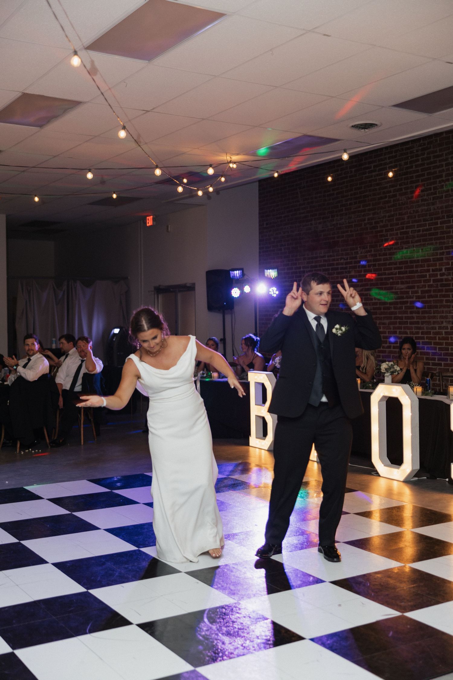 Couple dancing together on a black and white checkered dance floor with string lights and disco effects.