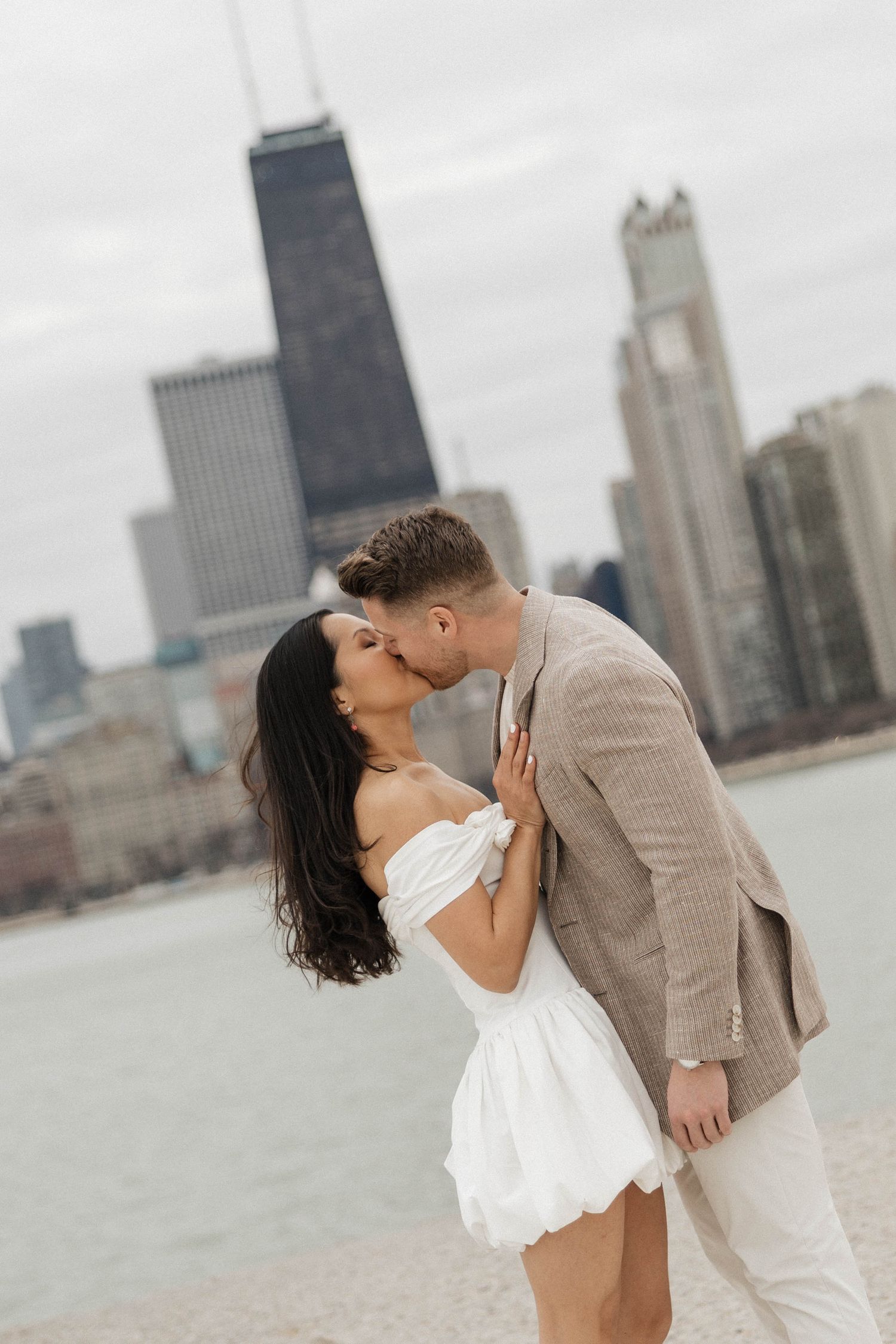 Couple sharing a romantic kiss on Chicago lakefront with city skyline and John Hancock Center in the background.