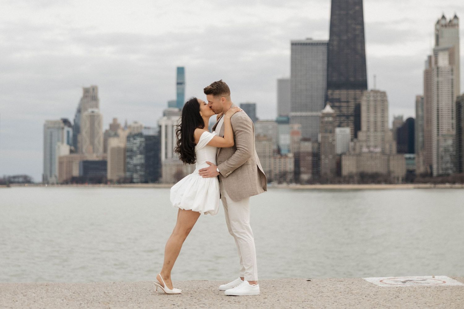 Romantic couple kissing on waterfront with Chicago city skyline on cloudy day.