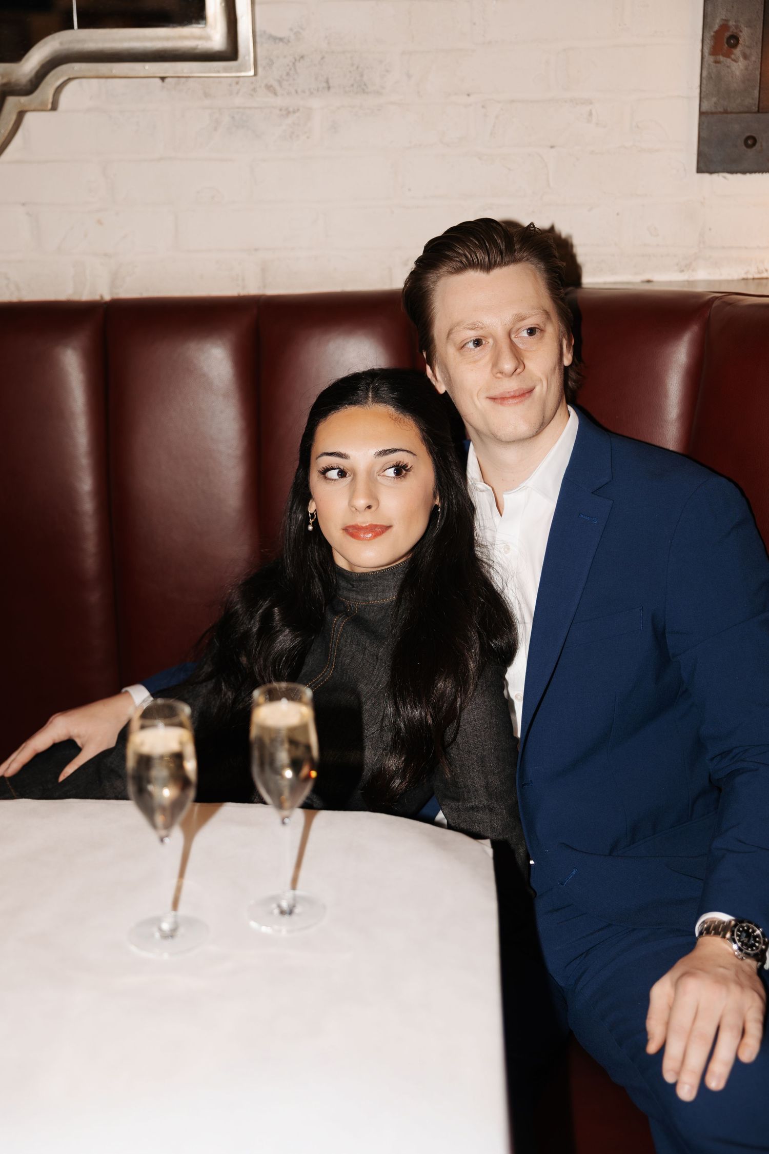 A couple sits together at a restaurant booth with champagne glasses on the table.