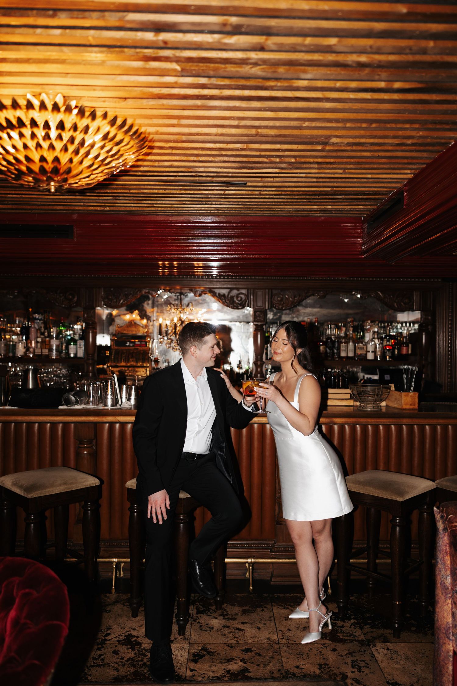 Couple enjoying drinks together at an elegant vintage bar with warm lighting and wooden decor.