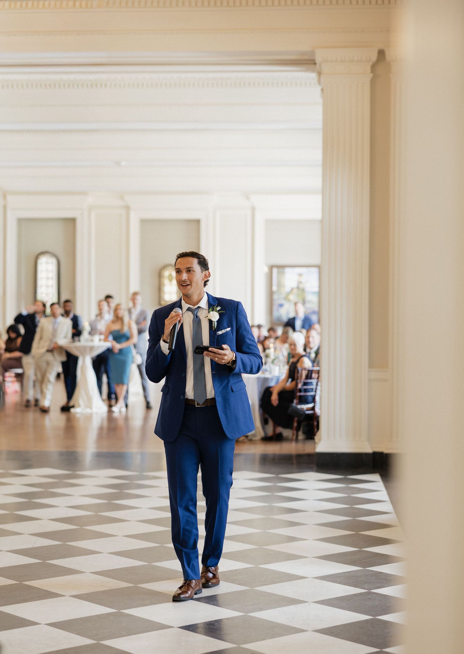 Person in blue suit walks across elegant black and white checkered ballroom floor in a grand venue.