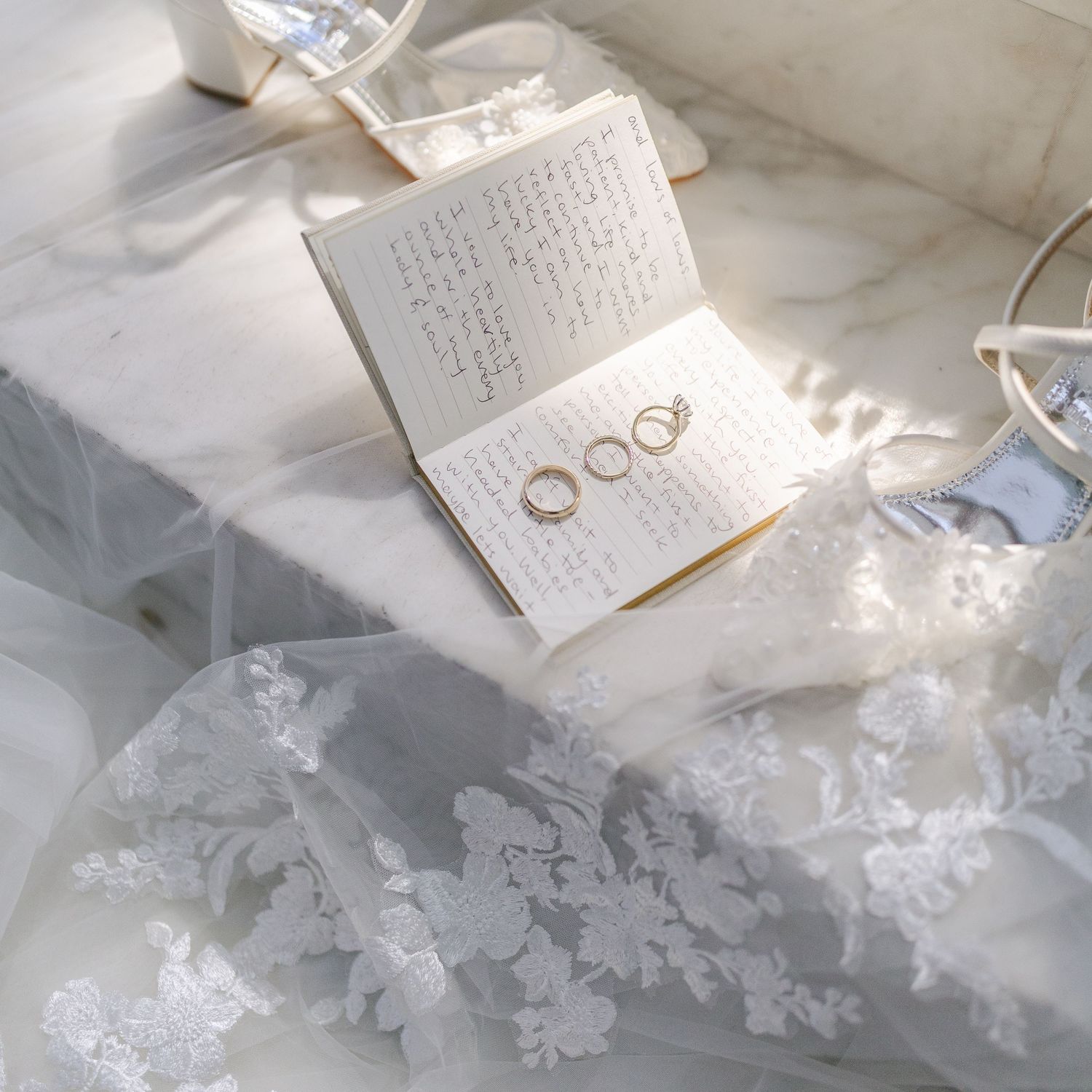 Handwritten wedding vows on paper with wedding rings and delicate white lace in soft natural lighting.