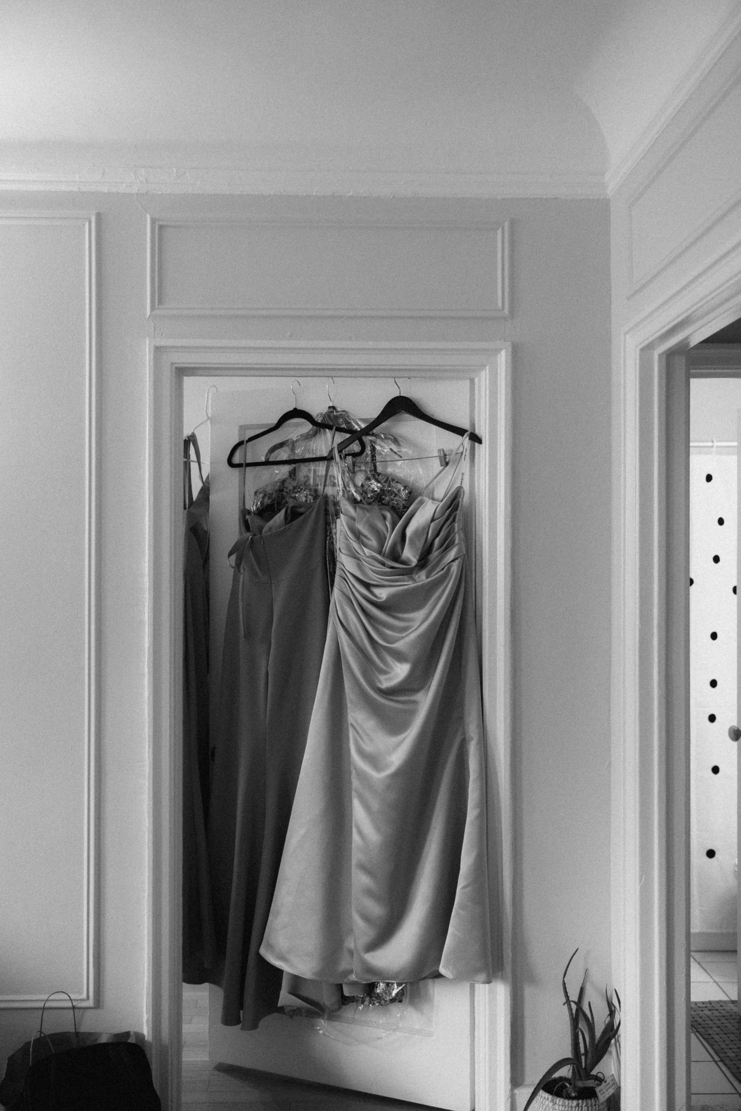 A series of black and white photographs showing hanging clothes and garments against white walls in minimalist settings.