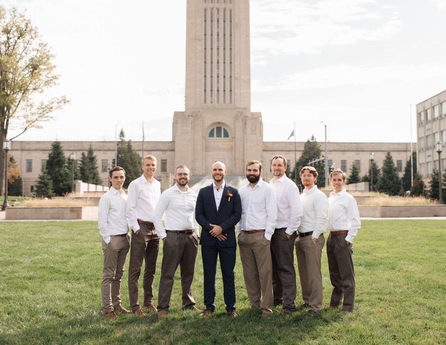 Groomsmen in coordinated attire pose for a formal group photo in front of a grand building.