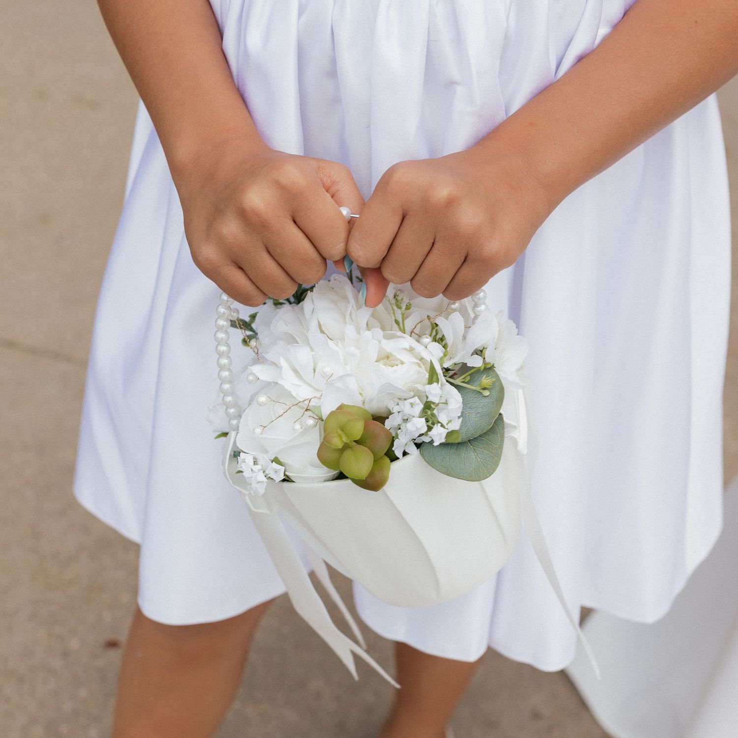 A white floral bouquet with eucalyptus leaves and green accents held against a white dress.
