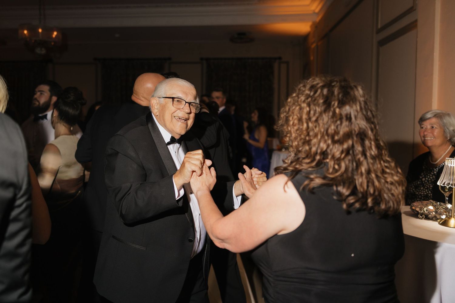 Elderly man in tuxedo dancing with a woman at a formal event or wedding reception.
