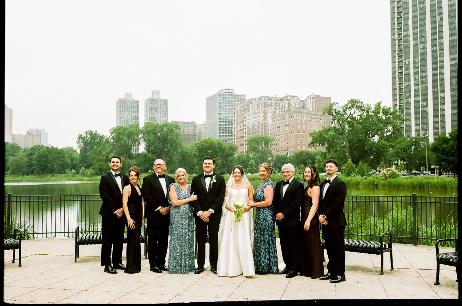 Wedding party poses by lakeside with Chicago skyline backdrop on overcast day.