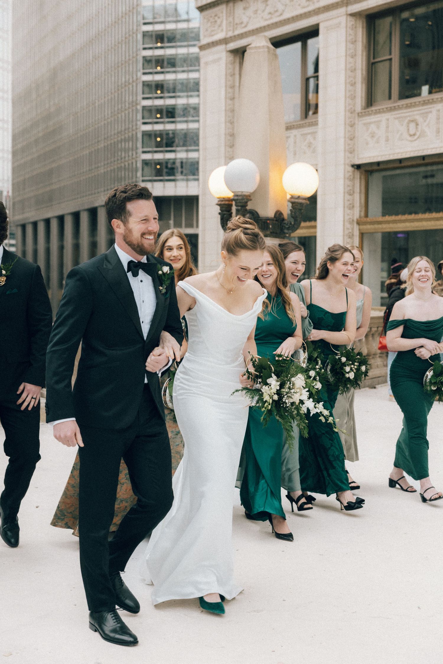 Wedding party members dance and twirl together in an elegant venue with marble columns and globe lights.
