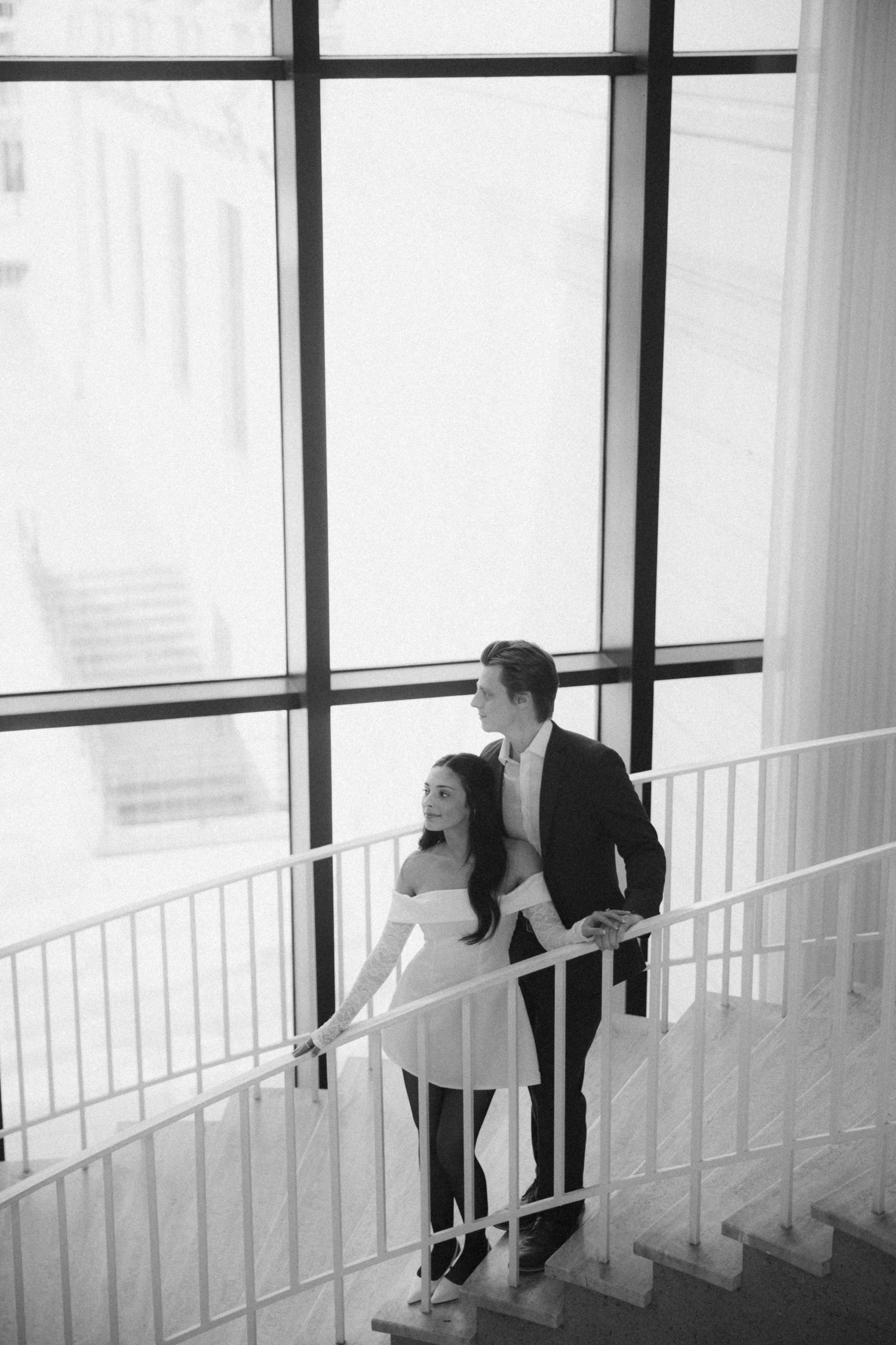 People in formal attire standing along a white railing in a bright interior space.