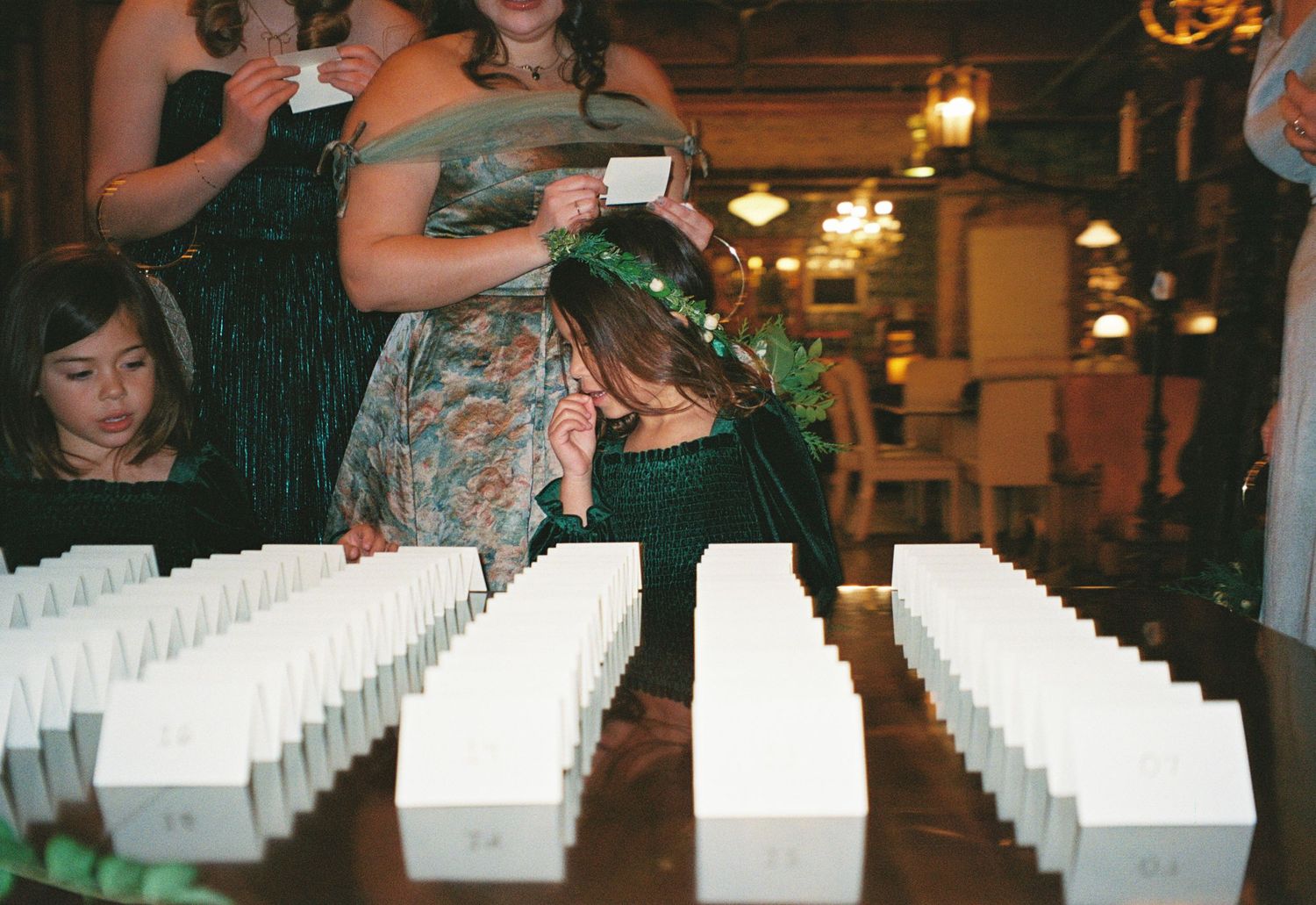 Wedding guests sign white cards at a reception table with glowing amber lighting in an elegant venue.