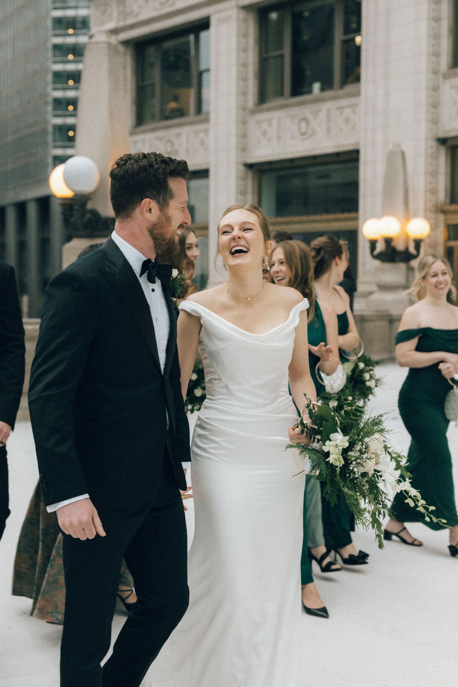 Joyful wedding couple shares a candid moment while dancing together outside an elegant stone building.
