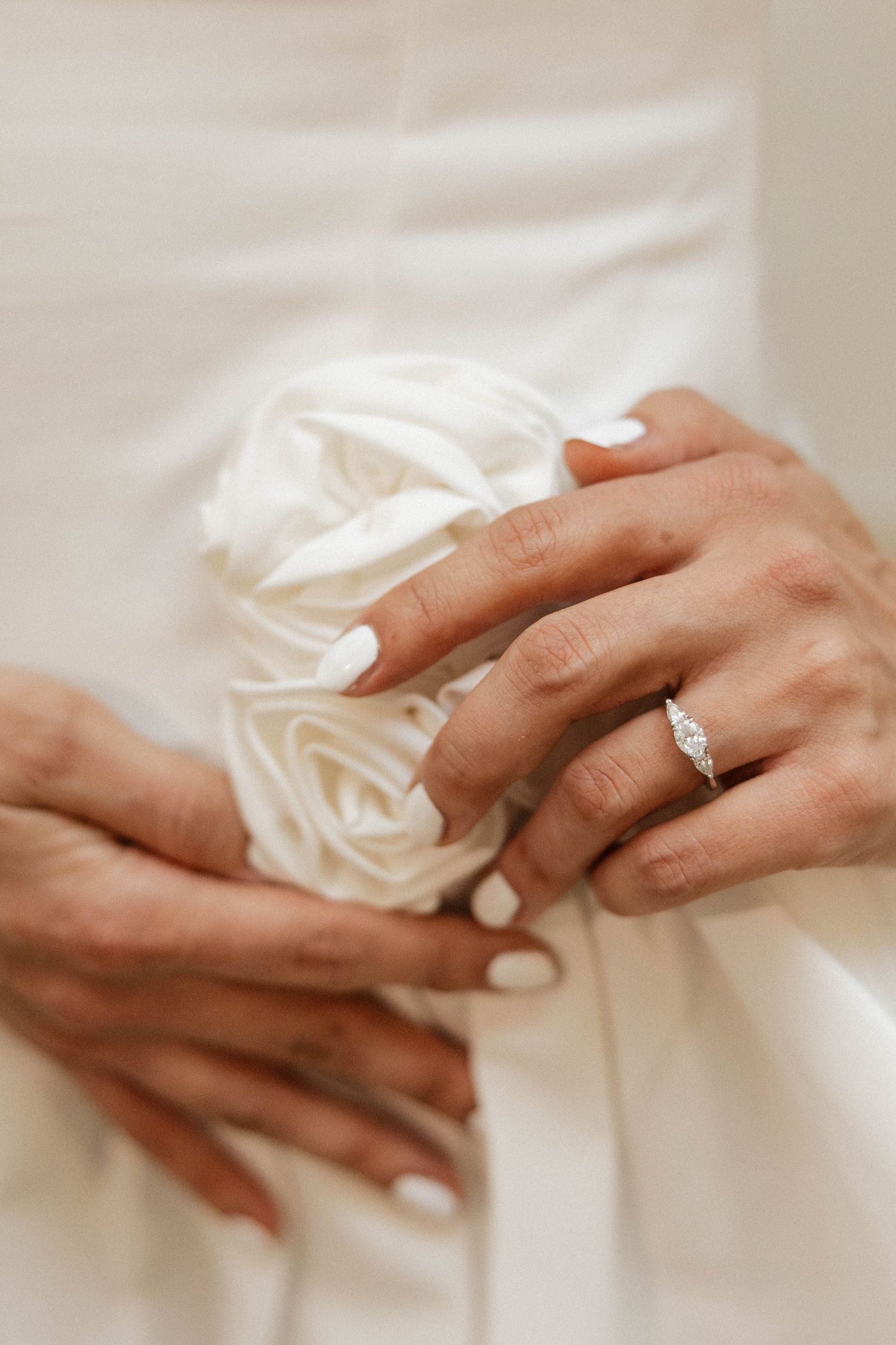 Close-up of bride's hands with white manicure and diamond engagement ring holding white roses.