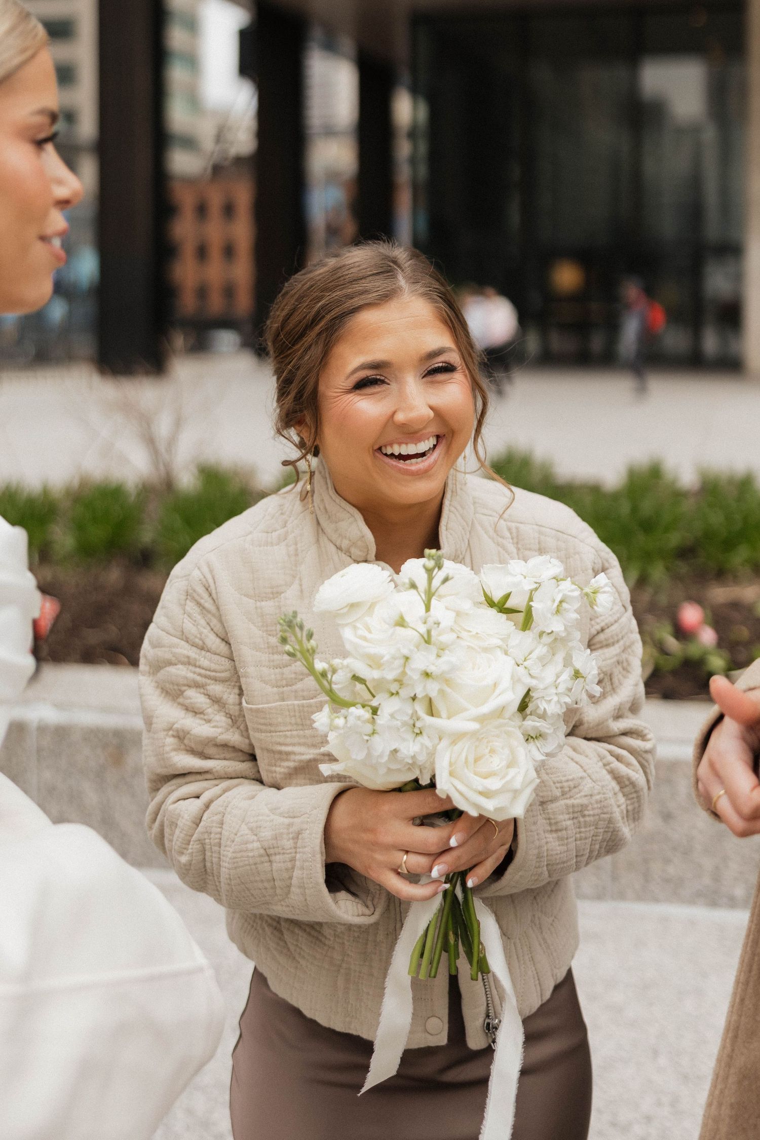 Smiling bridesmaid holds a white rose bouquet outdoors at a wedding celebration.