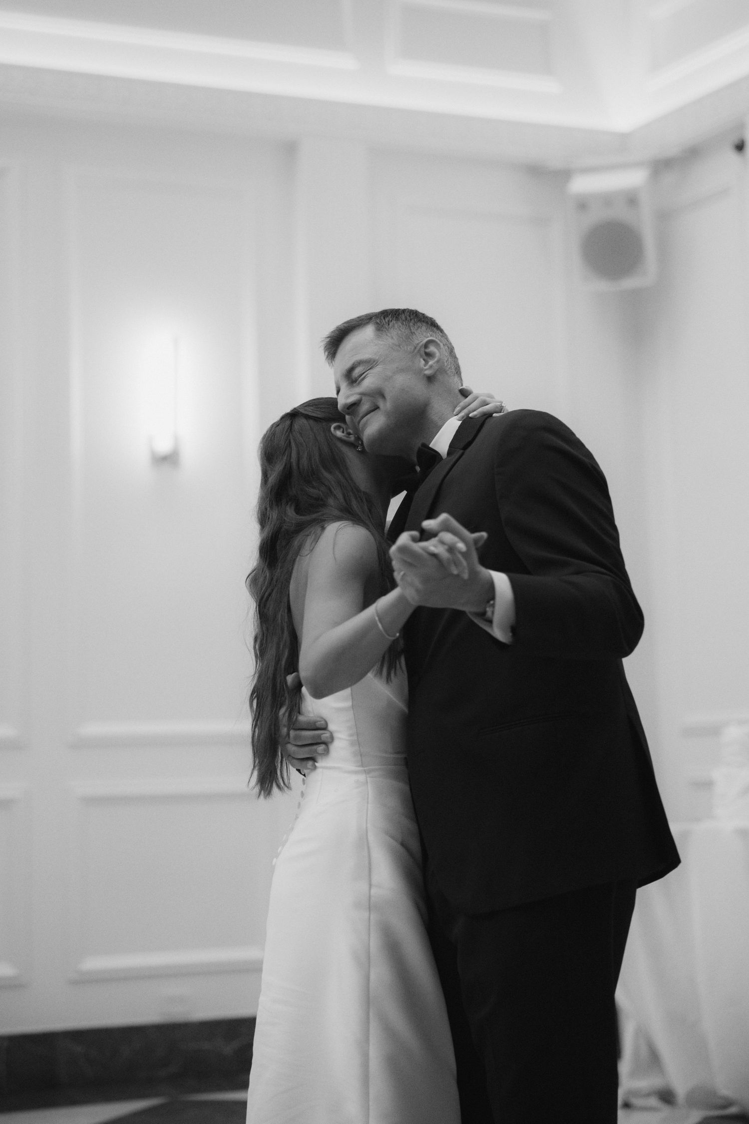 Black and white photo of a bride and groom sharing their first dance kiss at a wedding reception.