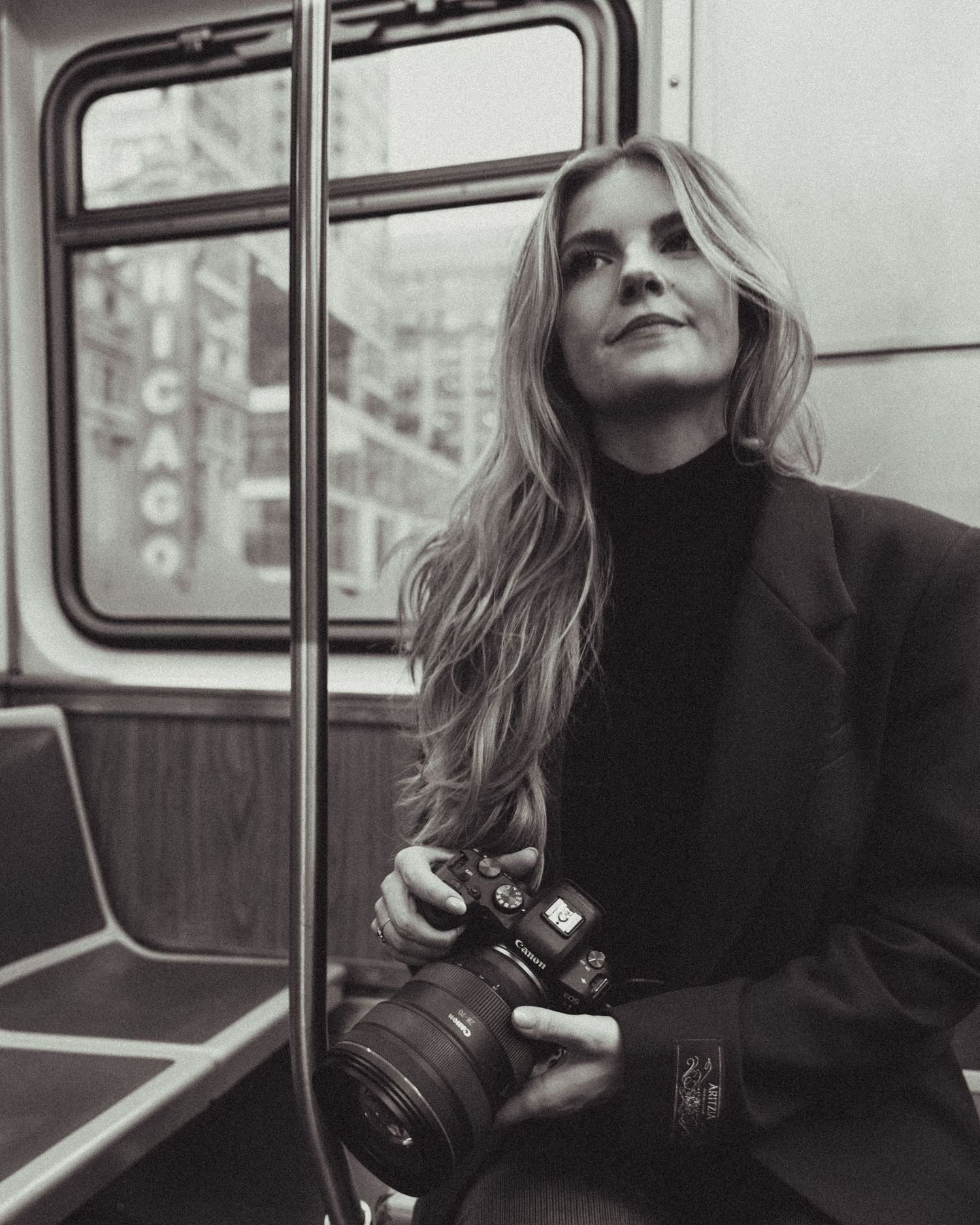 Woman with long blonde hair holds a camera on a subway train in Chicago, captured in black and white.