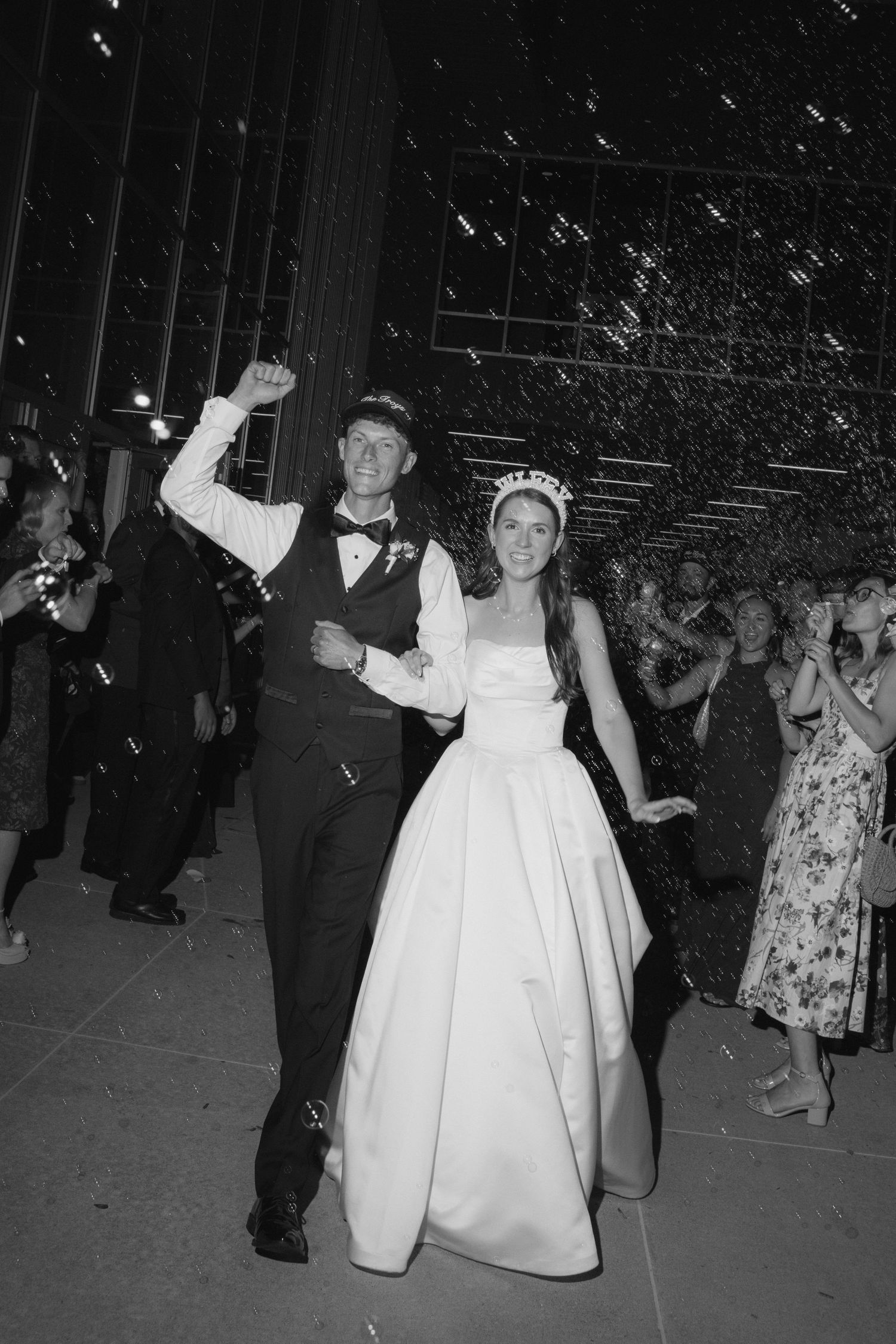 Black and white photo of a joyful bride and groom celebrating their wedding exit with confetti and cheering guests.
