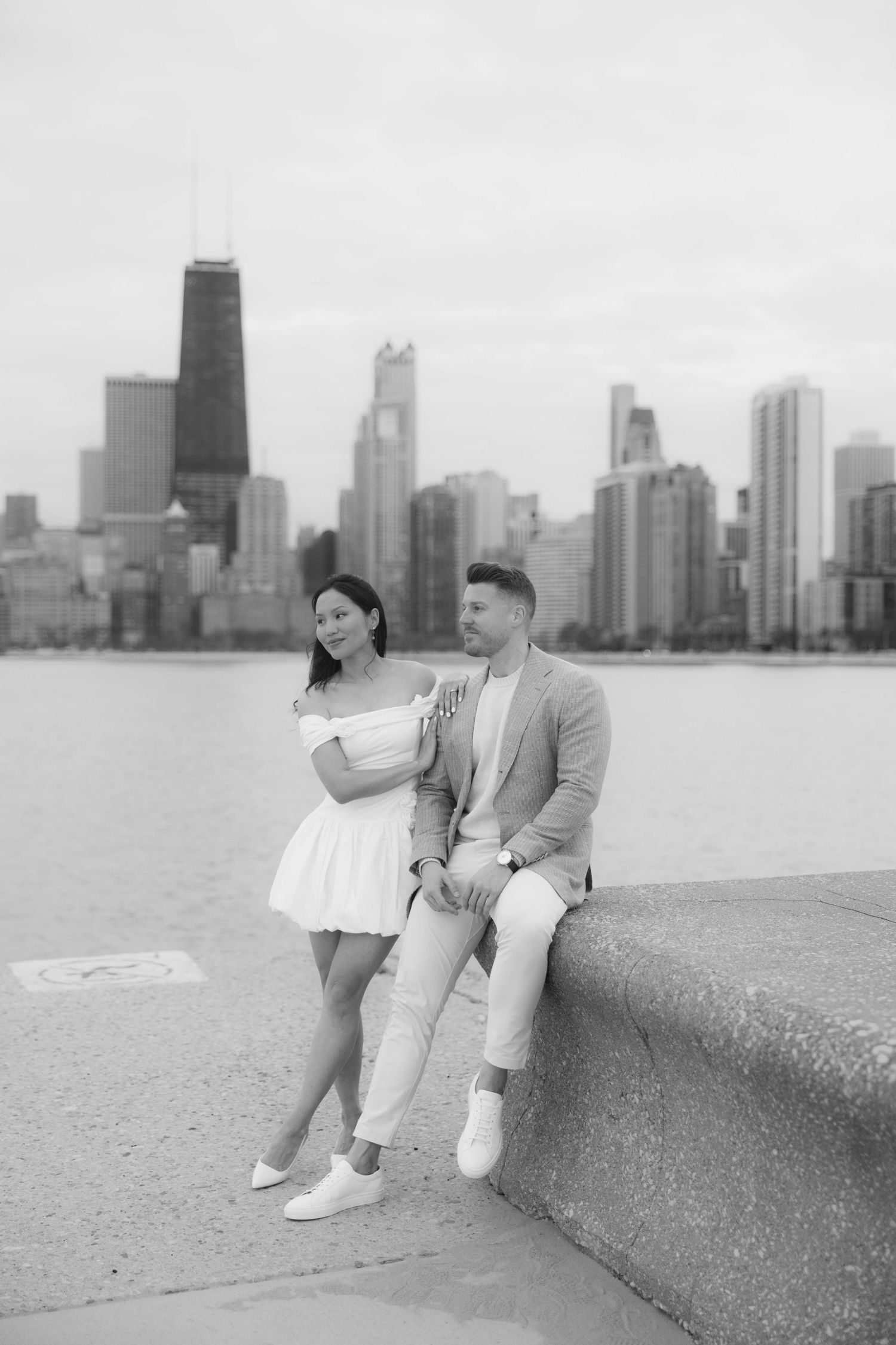 Black and white photo of a couple posing by the Chicago lakefront with the city skyline in the background.