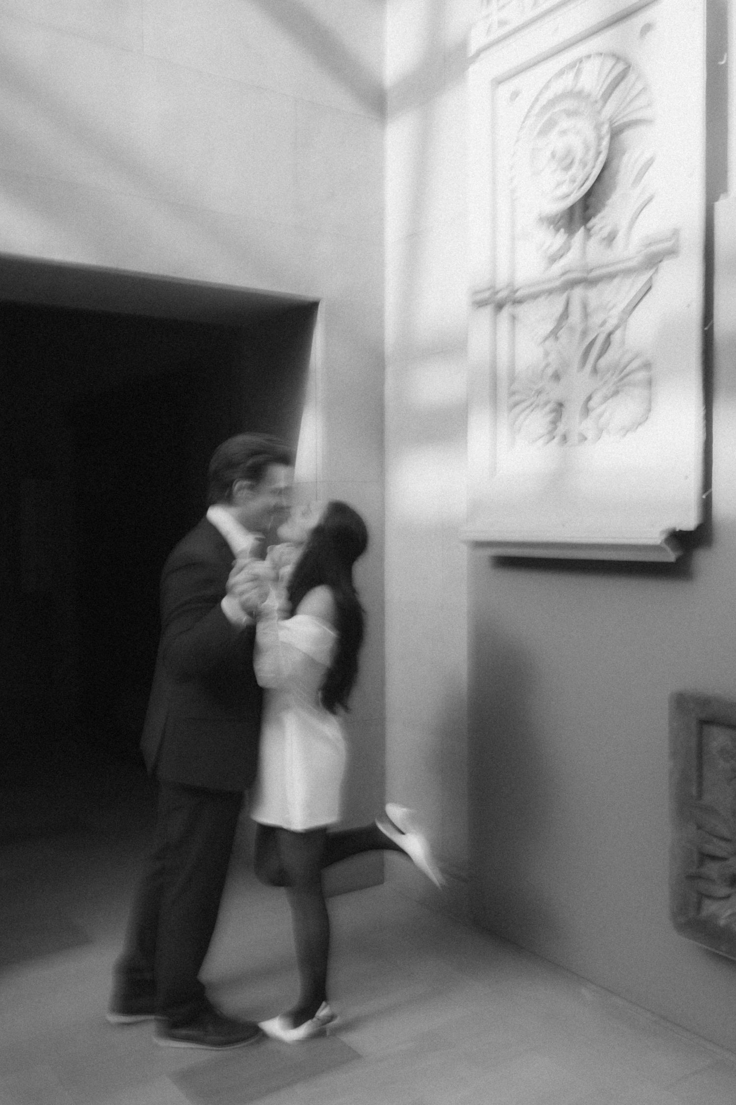A romantic couple shares an intimate dance in a modern gallery setting with white walls.
