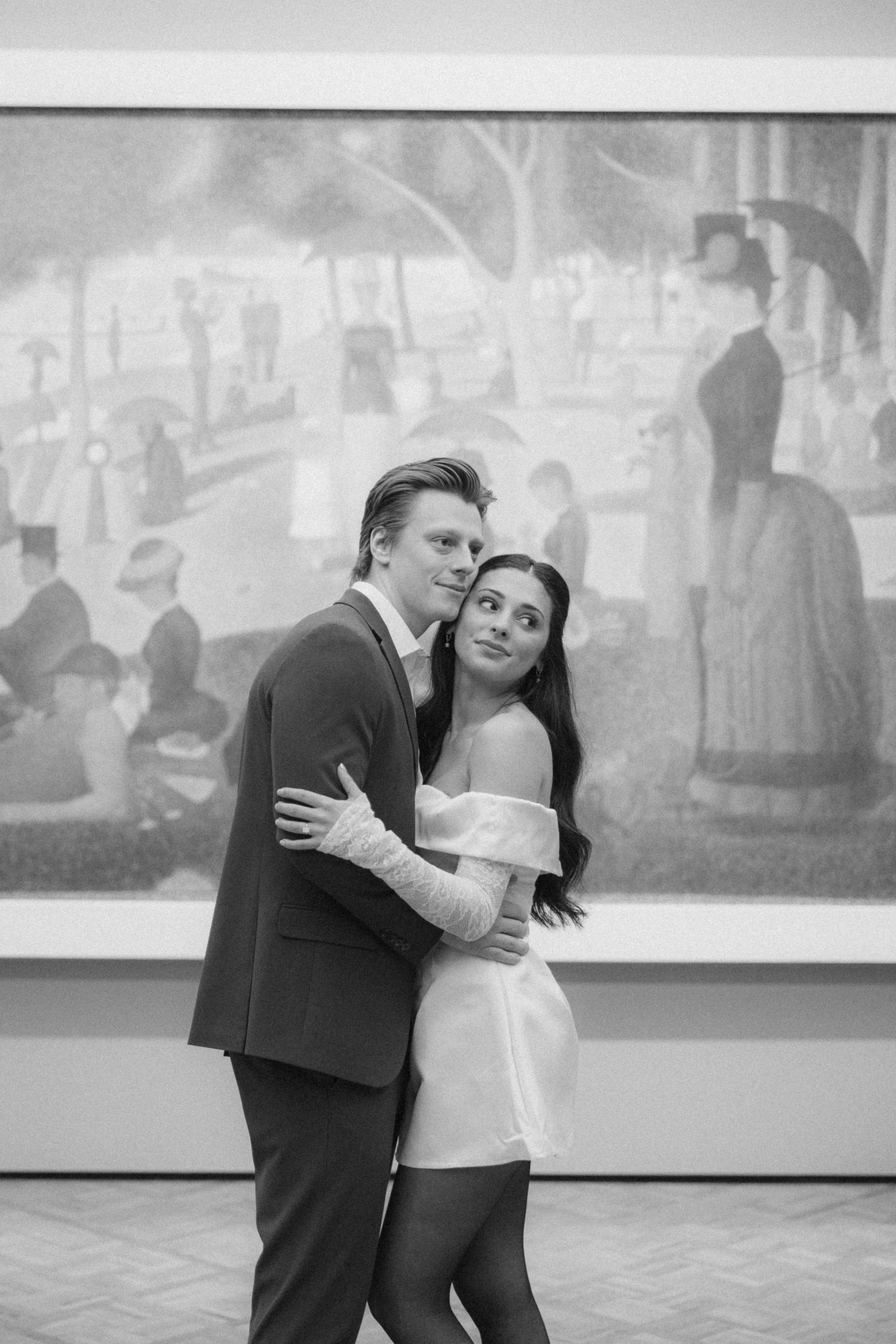 A romantic couple dancing and embracing in a gallery space with artwork on the walls.