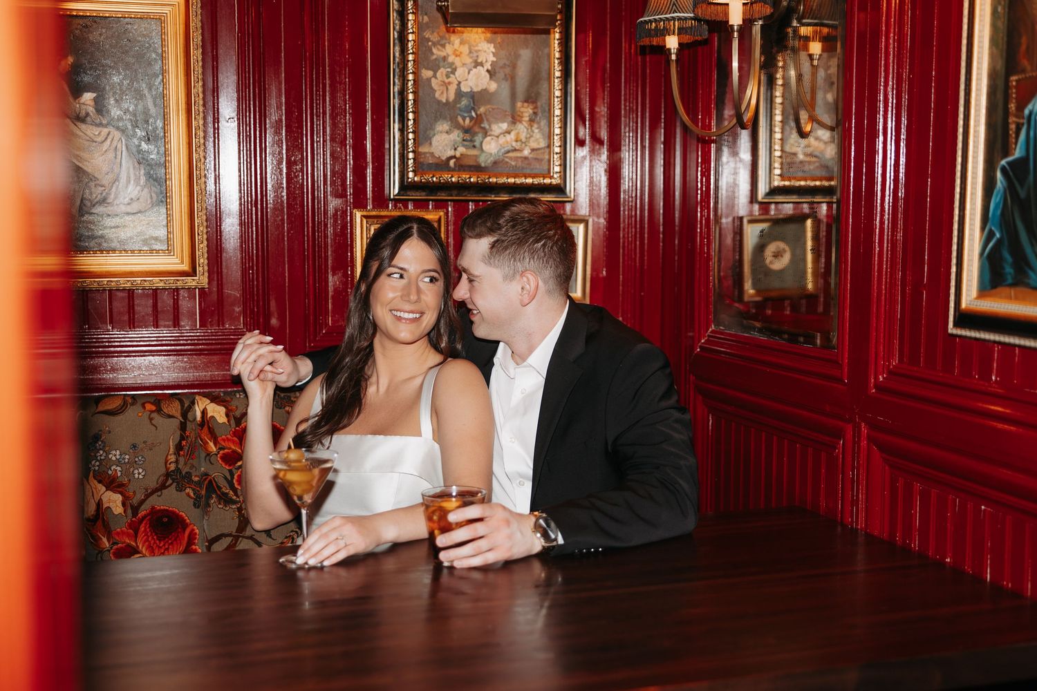 Wedding couple shares a drink together at an elegant venue with rich red wood-paneled walls and framed artwork.