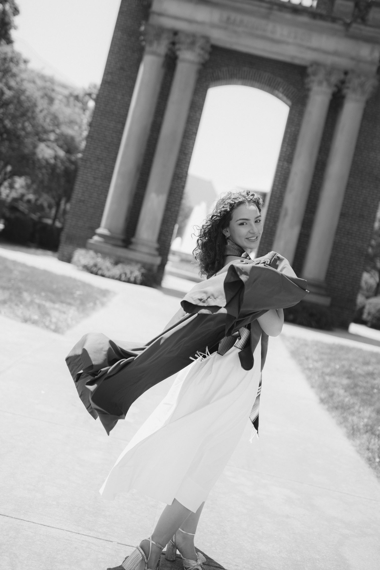 A graceful dancer in a white dress twirls and spins under a columned archway in a series of black and white photos.