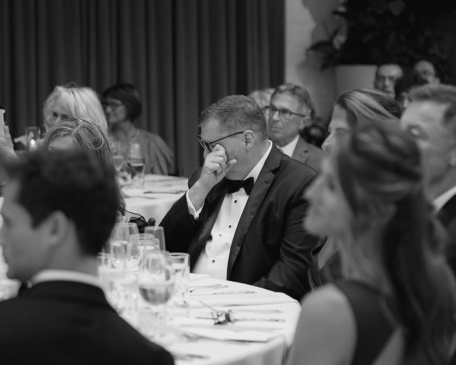 Black and white photo of guests in formal attire seated at tables during an elegant gala or wedding reception.