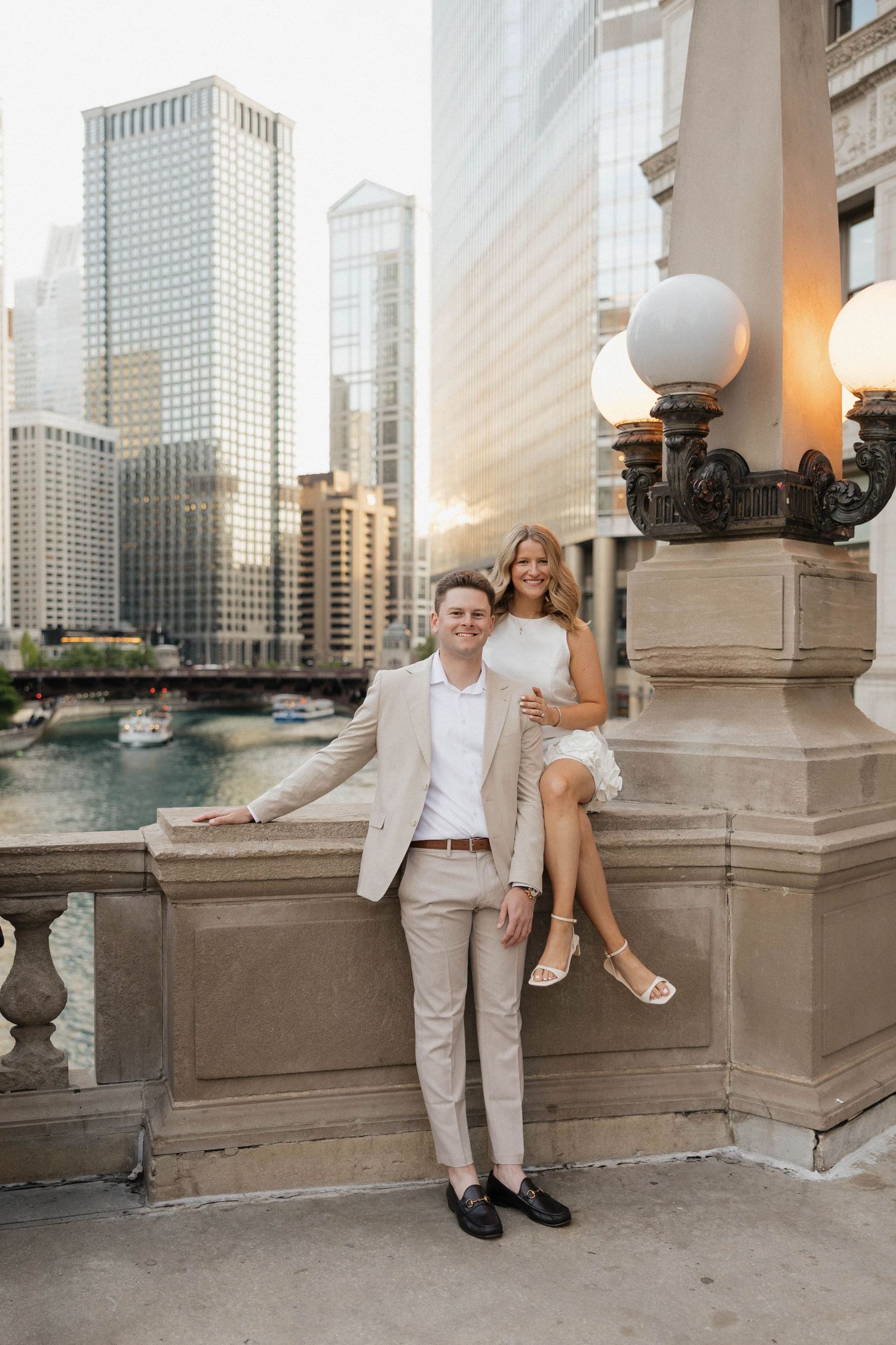 Couple posing on a bridge overlooking the Chicago River at sunset, man in beige suit, woman in white dress.