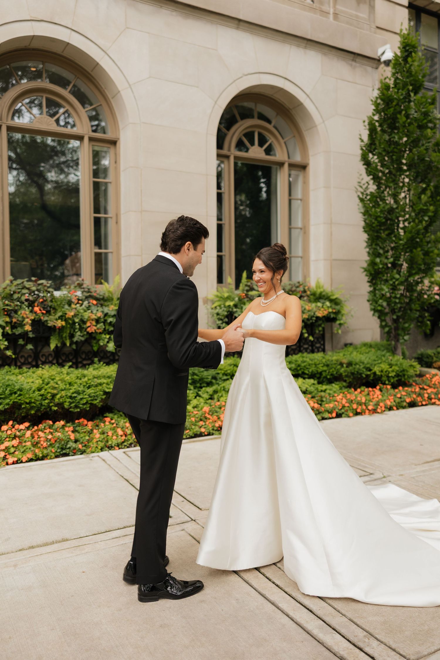 Bride and groom share a tender first look moment outside an elegant stone building with lush greenery.