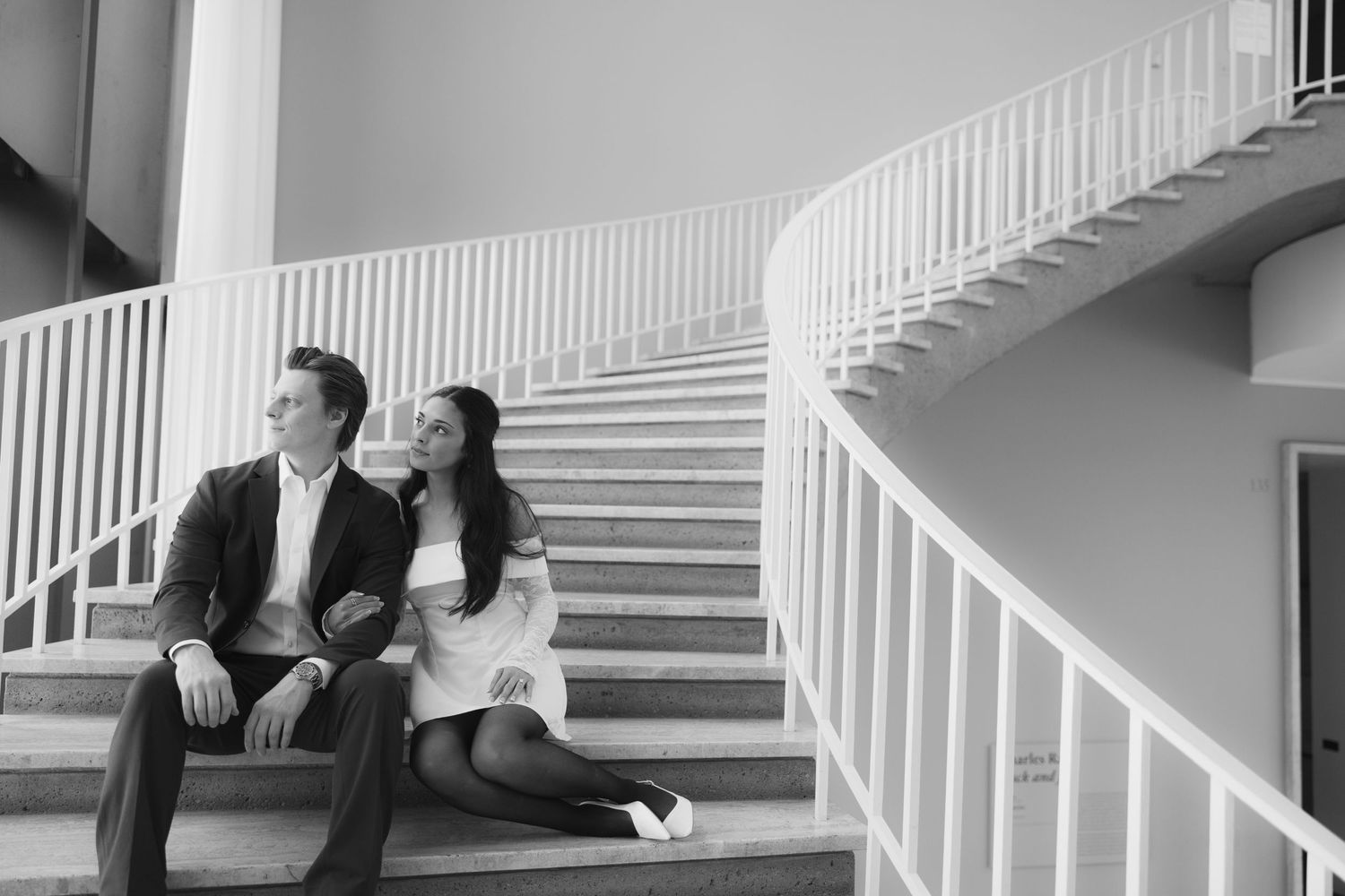 Black and white photo of couple posing on elegant white staircase.