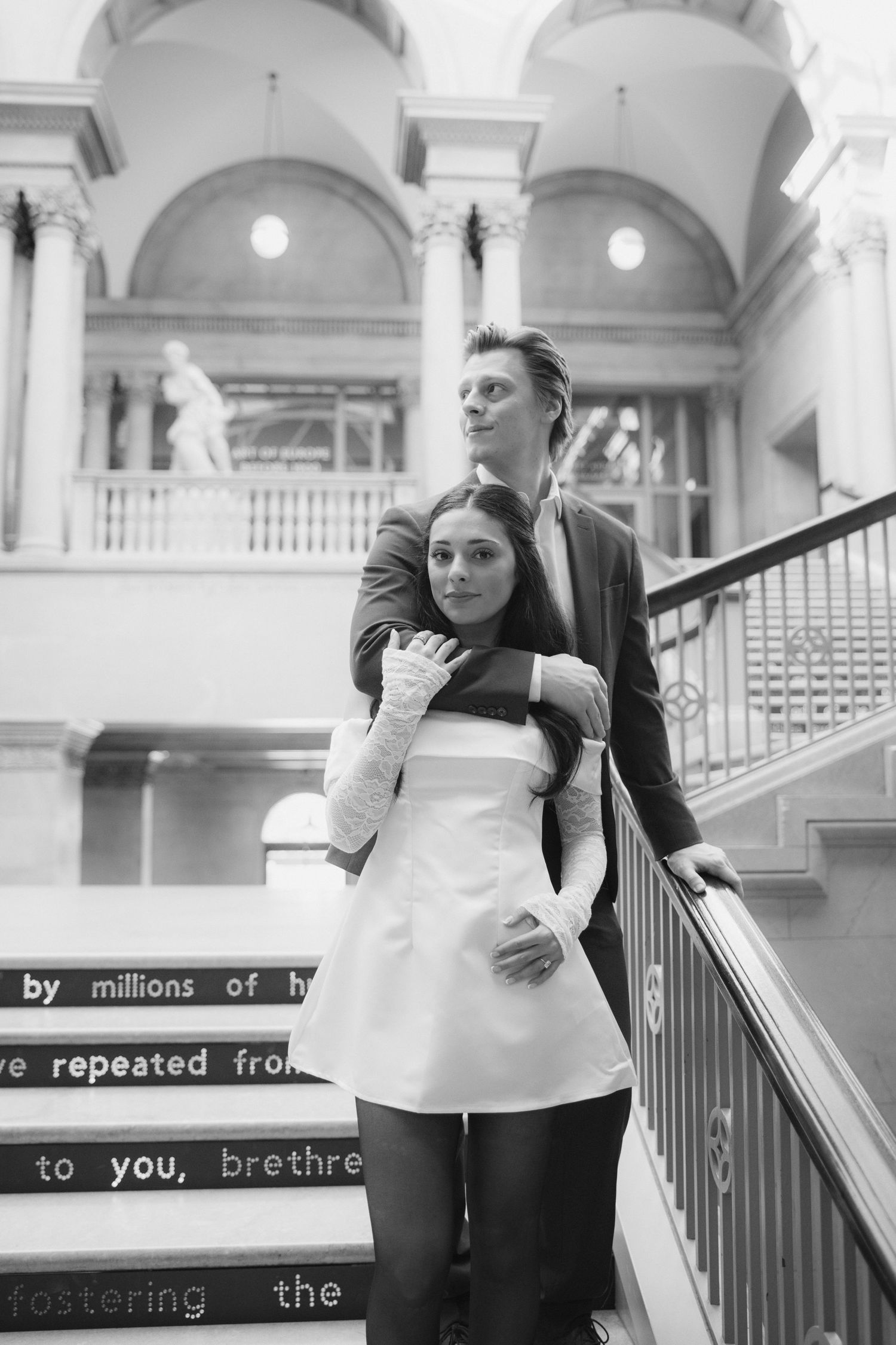 Two people pose together in a grand hallway with classical architecture and arched ceilings.