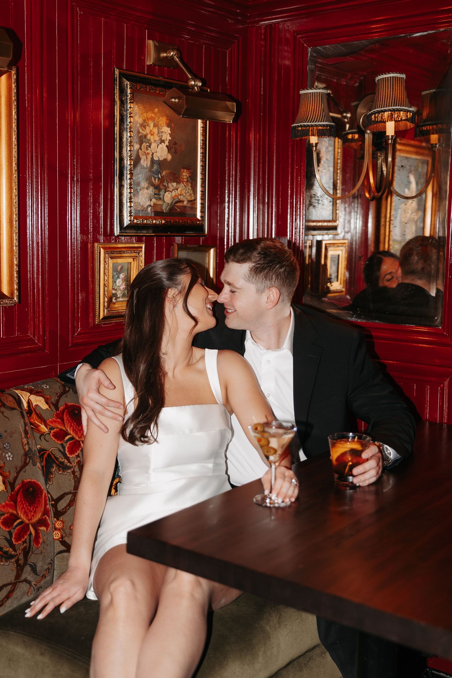 A couple shares an intimate moment at a vintage-style bar with red walls and ornate decor.