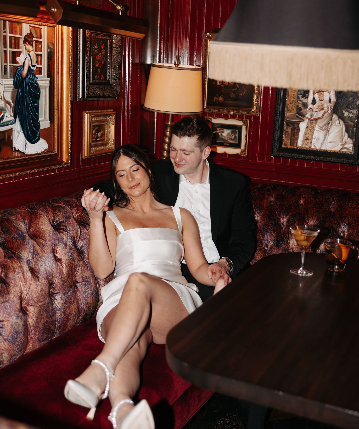 A tender moment captured in an elegant bar setting with antique frames and plush red seating.