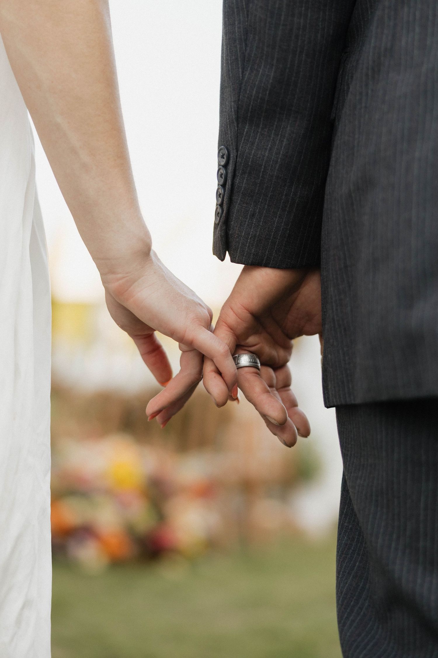 Close-up of bride and groom holding hands, groom wearing silver wedding band, dressed in white gown and dark suit.