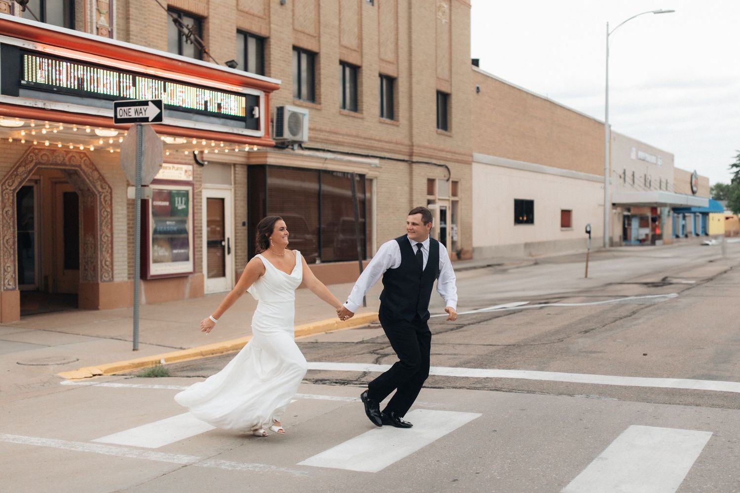 A couple in wedding attire poses for photos on an urban street with brick buildings in the background.