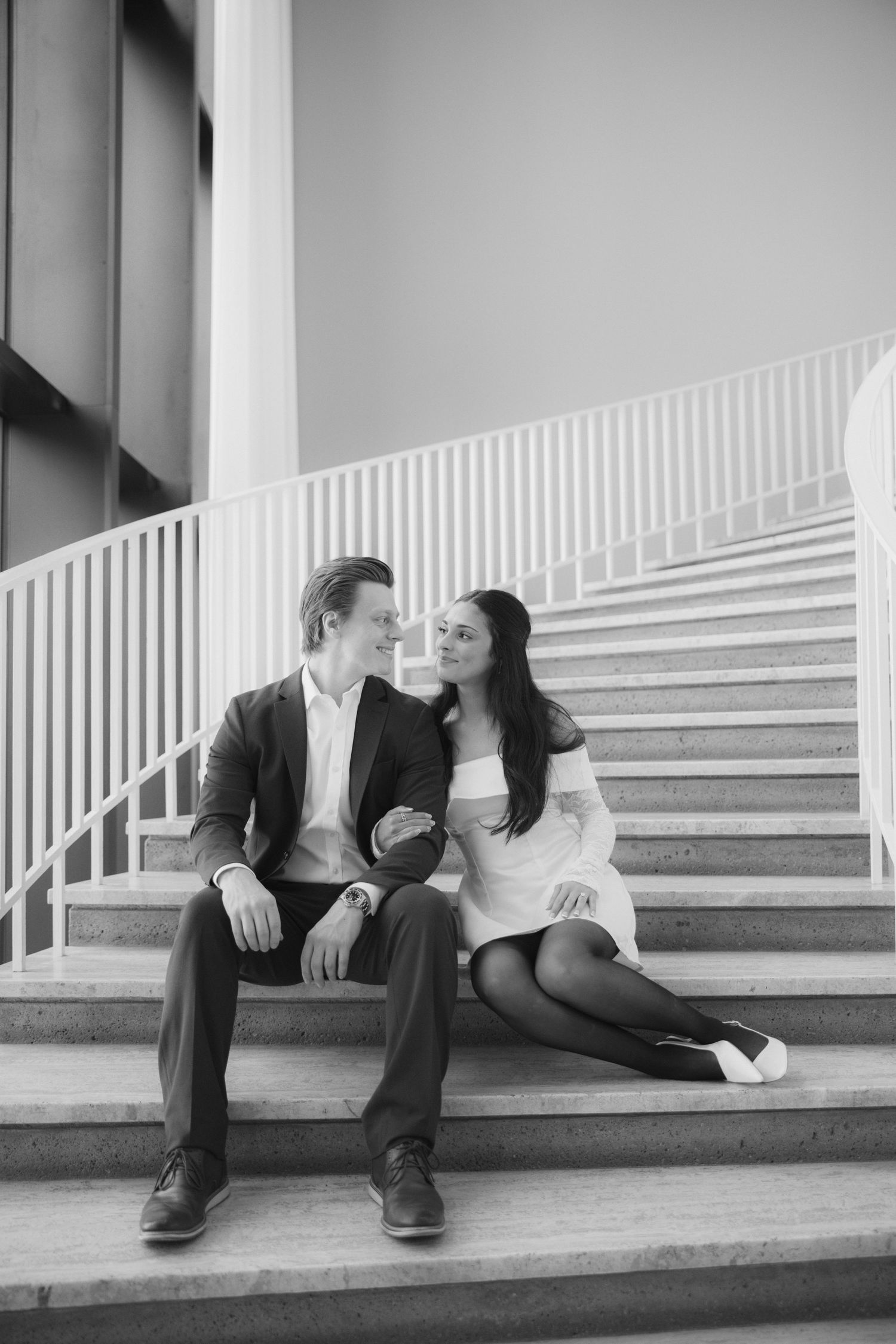 A black and white photo of a couple sharing a tender moment while sitting on modern stairs.