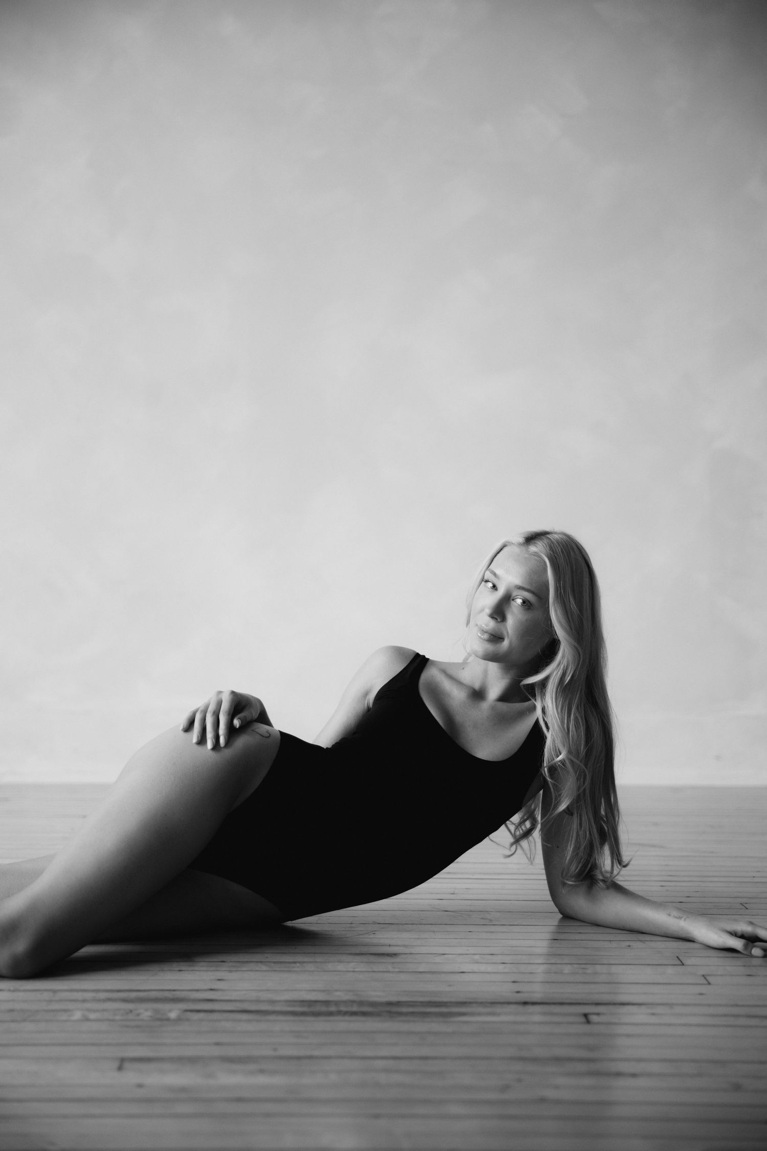 Artistic black and white photo series showing a figure in dark clothing reclining on a wooden floor in different poses.