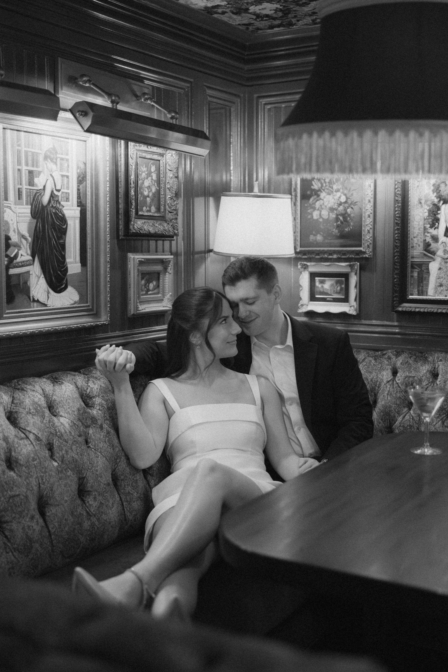 A romantic black and white photo of a couple in formal attire sharing an intimate moment on a tufted banquette.