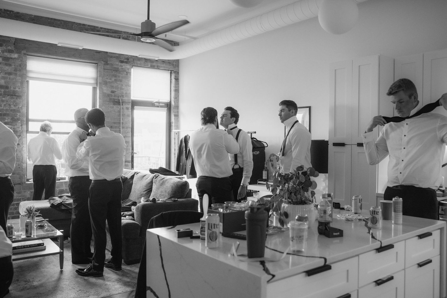 Black and white photo of groomsmen getting ready in a stylish loft space before a wedding ceremony.