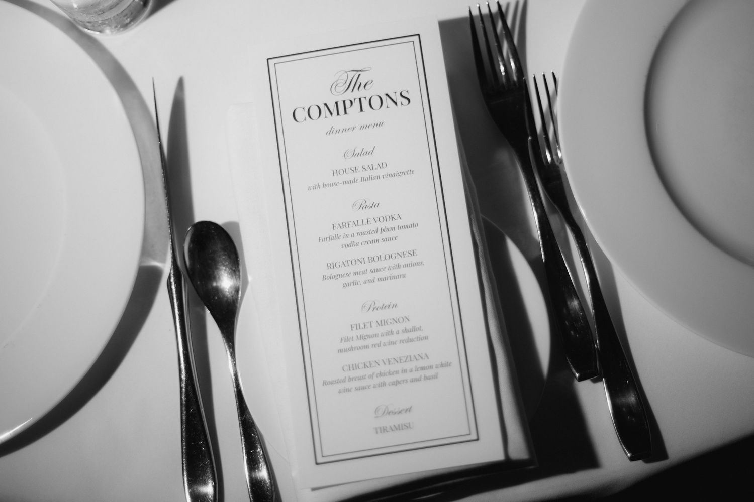 Black and white photo of The Comptons dinner menu on a formal table setting with silverware and plates.