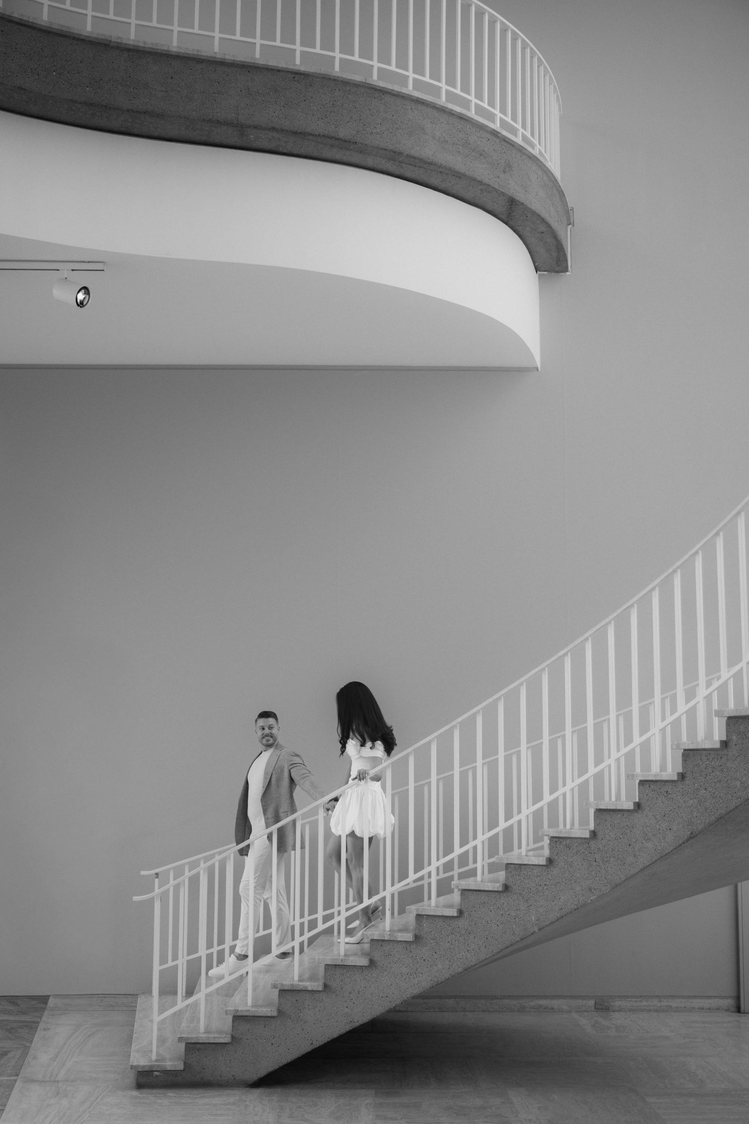 Black and white photo of a couple on a curved spiral staircase inside a modern building.