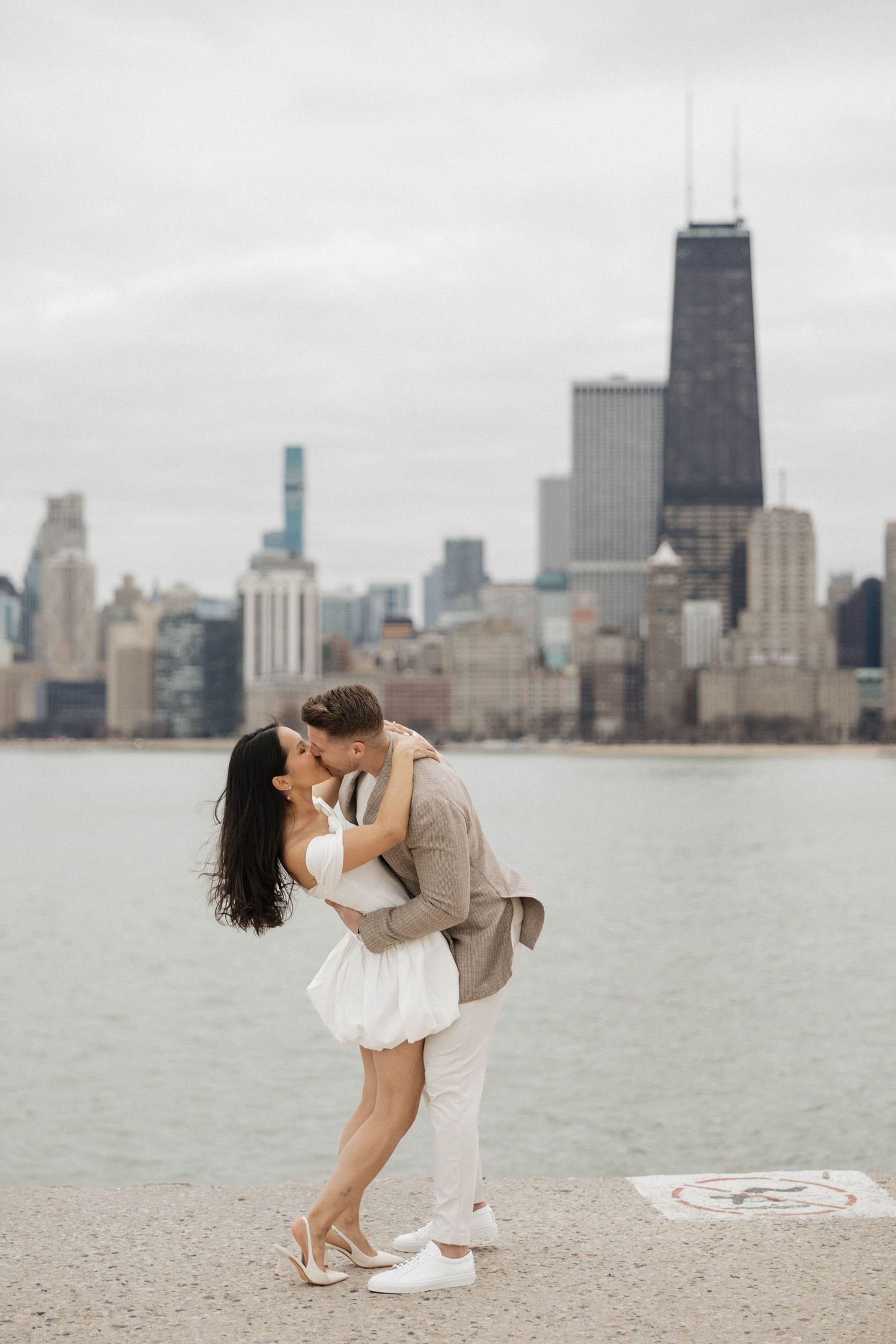 Couple sharing a romantic kiss by Lake Michigan with Chicago skyline backdrop.