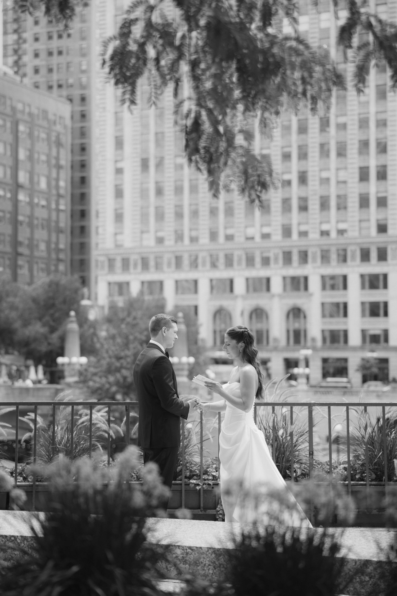 Black and white photo of a bride and groom exchanging vows outdoors with city skyscrapers in the background.