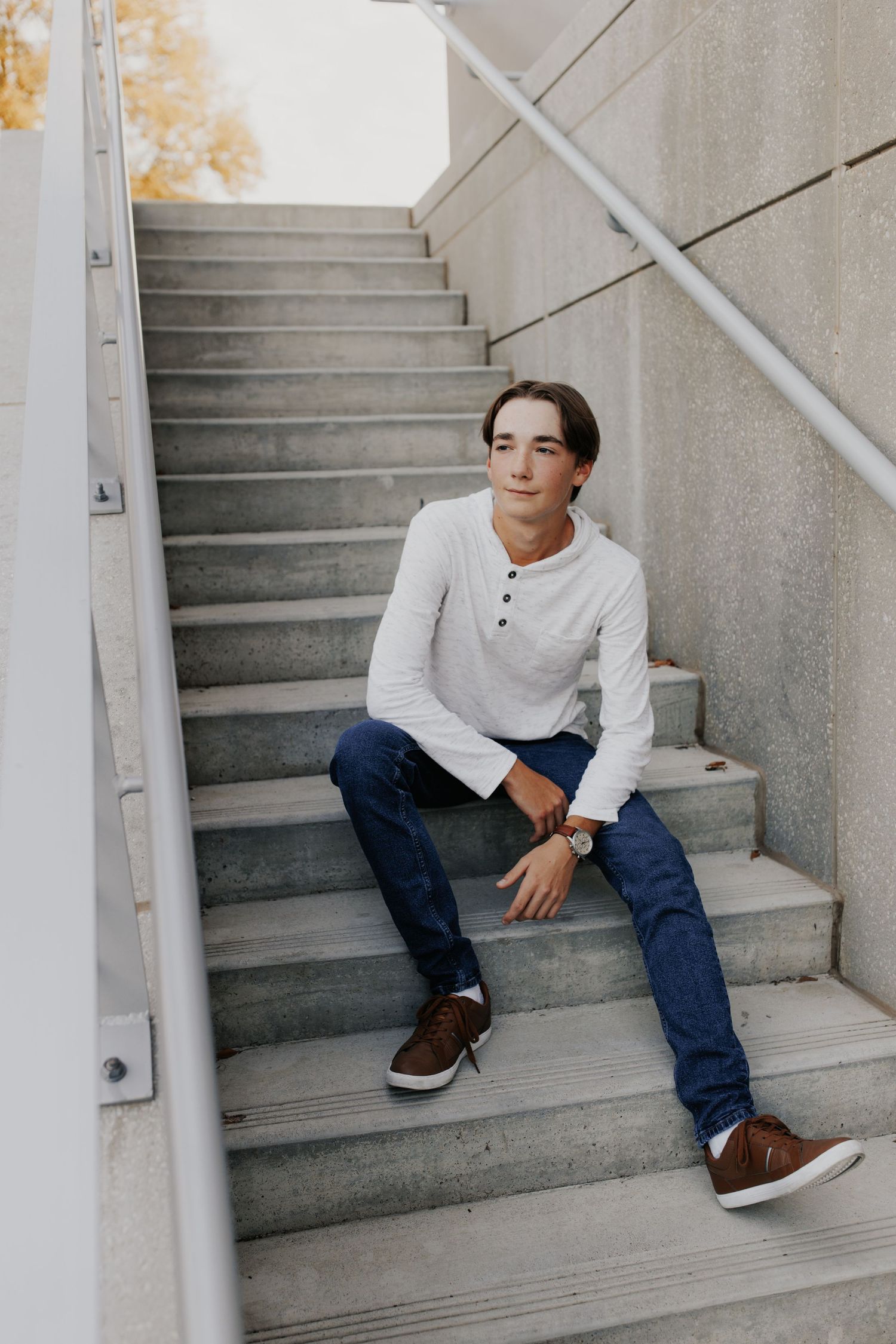 Casual portrait of someone sitting on concrete steps wearing jeans and a white henley shirt.