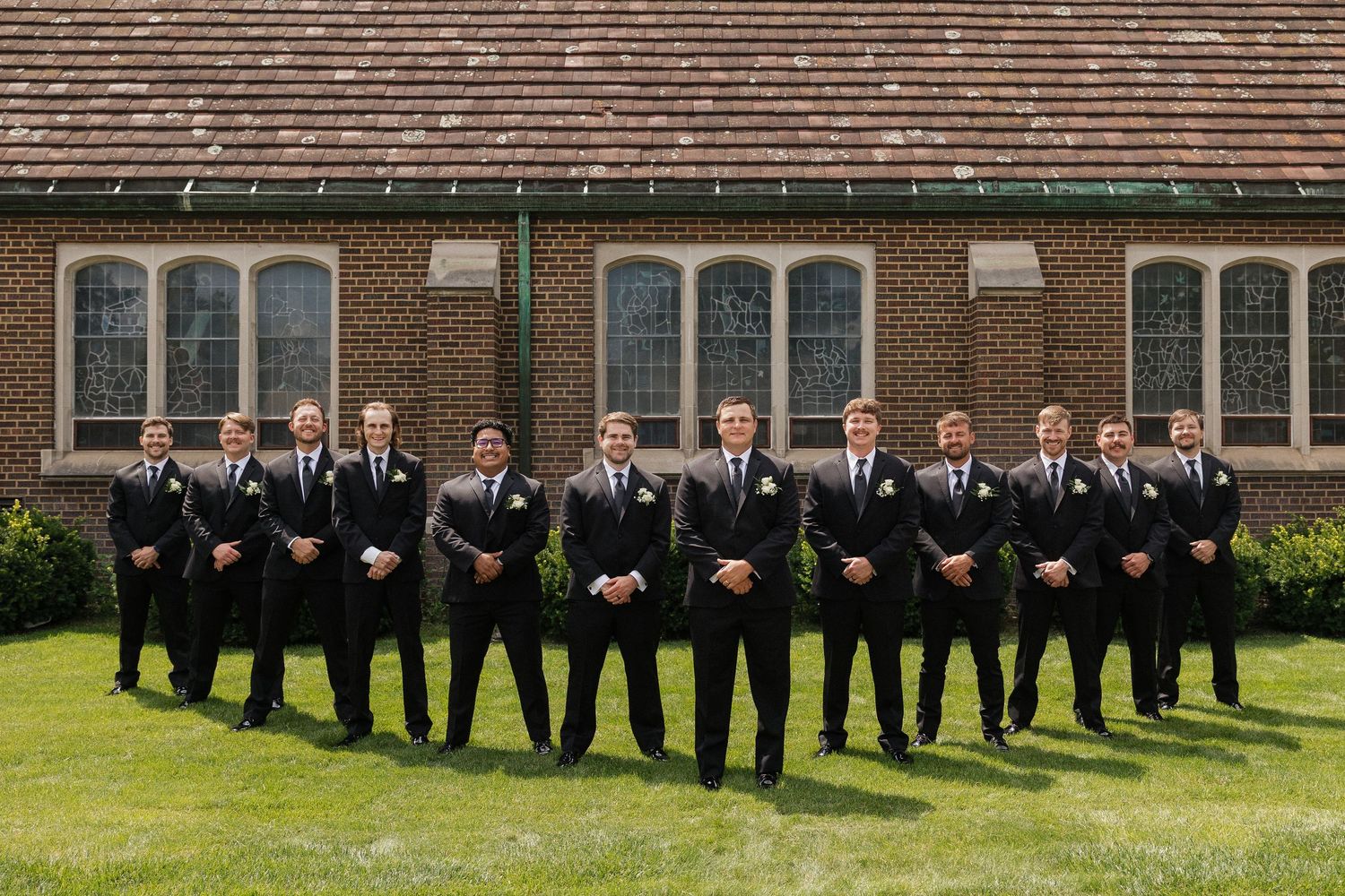 Wedding party members in formal attire lined up outdoors against a brick building.