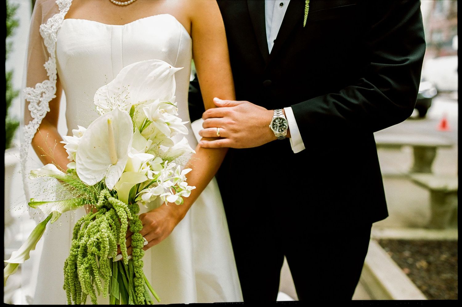 Bride in white strapless gown holding calla lily bouquet stands beside groom in black tuxedo at wedding ceremony.
