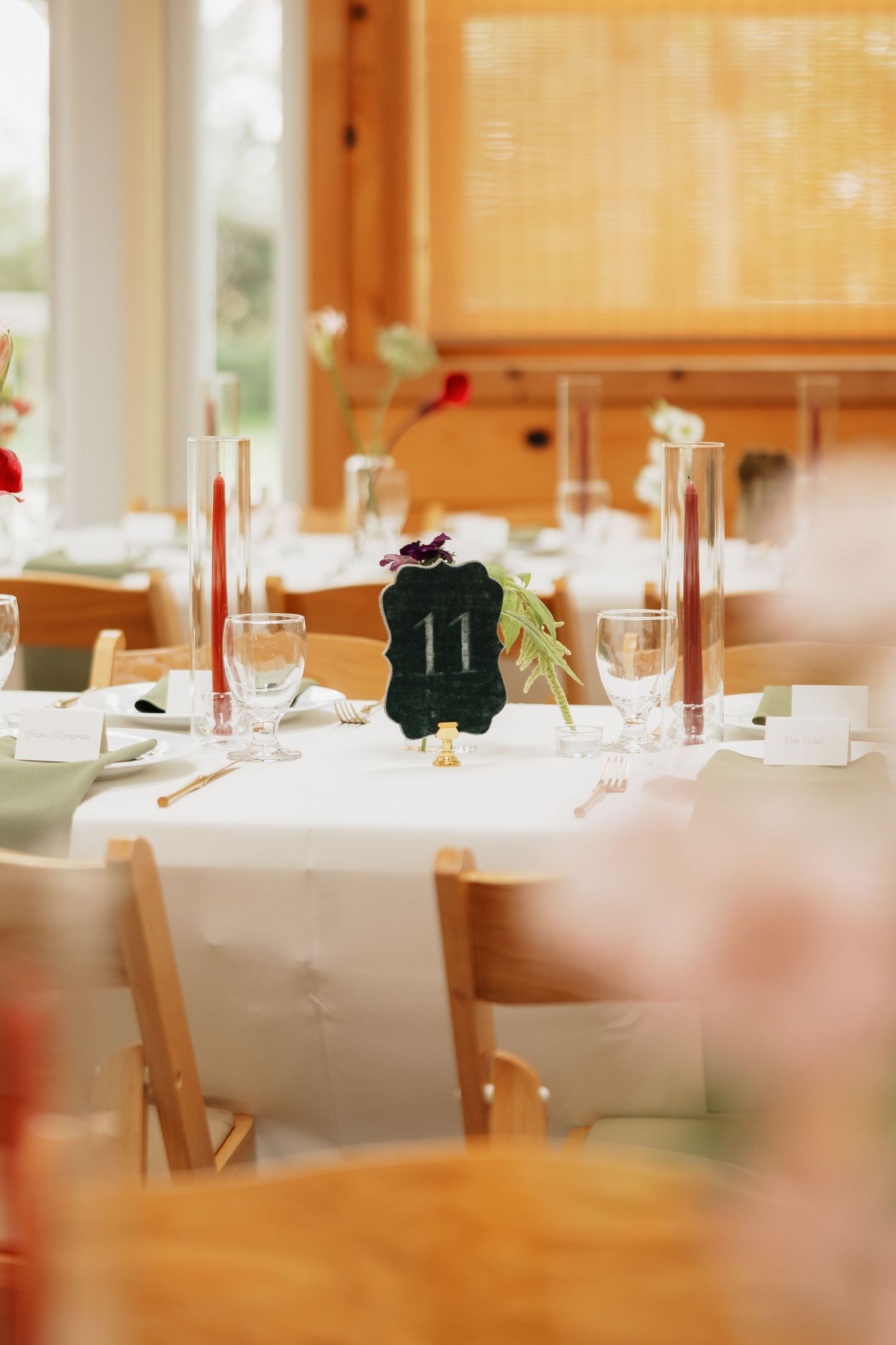 Elegant wedding reception table with white linens, table number 11 sign, tall candles, and glassware in a bright wooden venue.