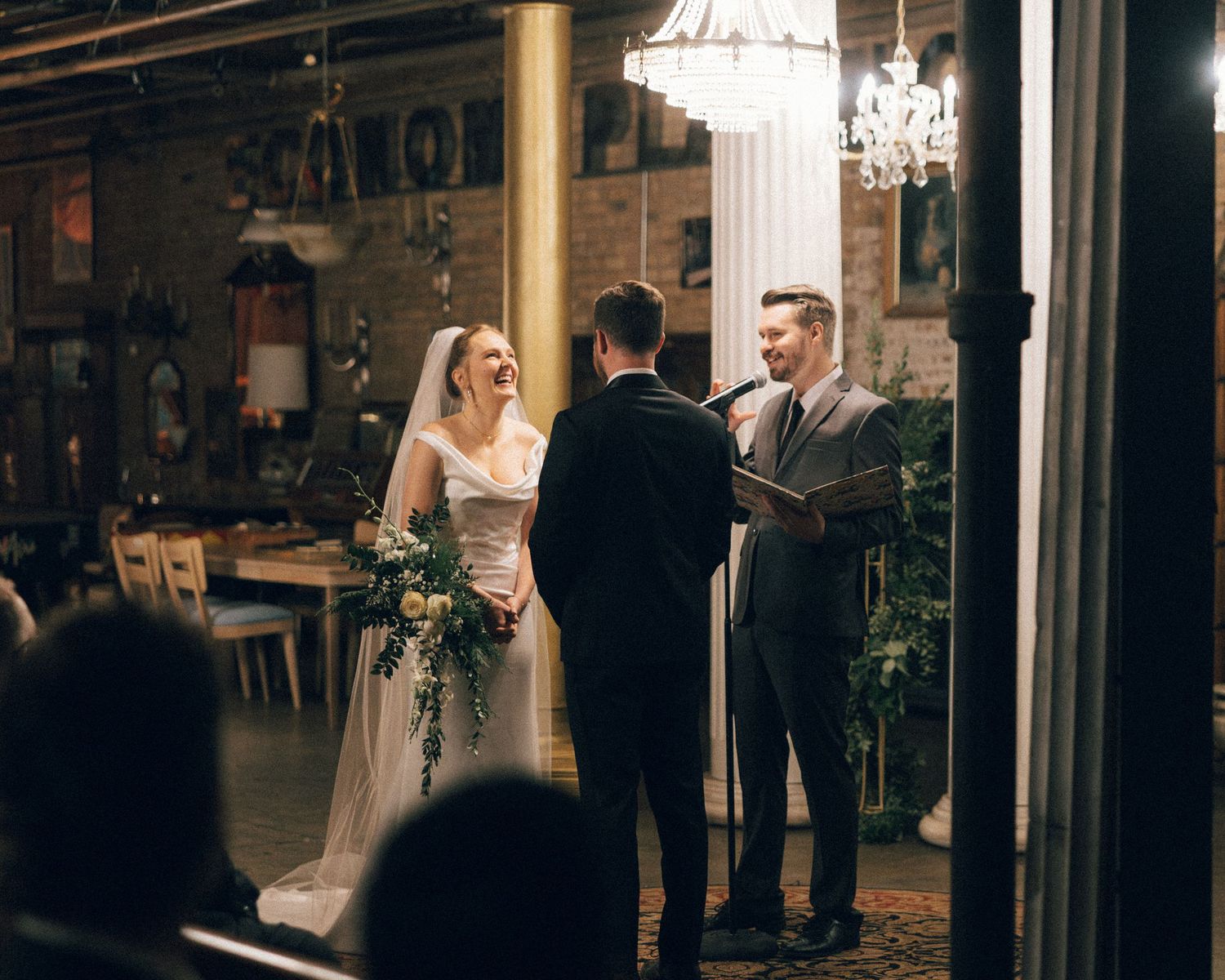 Wedding guests gather in an elegant indoor venue with glass walls and dark wooden accents during an evening reception.