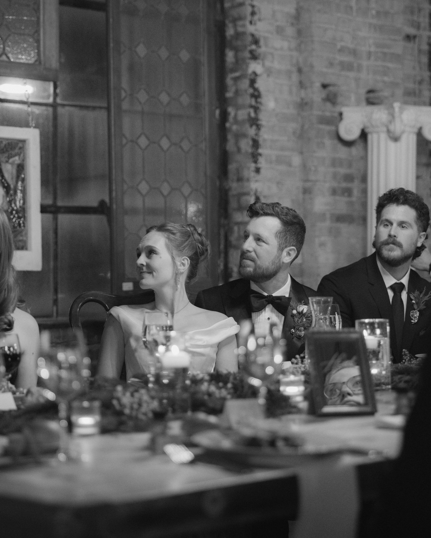 Black and white photo of guests seated at a formal dinner table with candles and place settings.